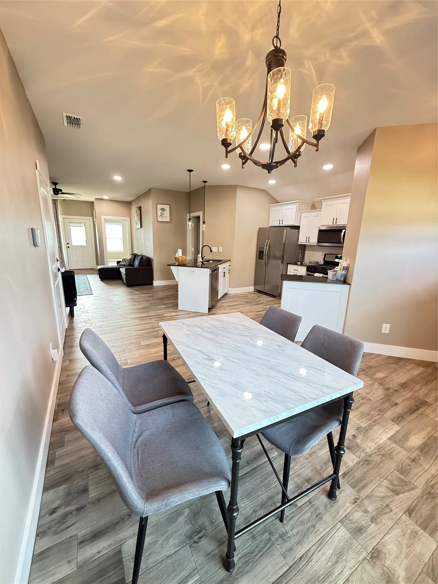 Open concept living space featuring wood-finish flooring, a kitchen with white cabinetry and stainless steel appliances, a dining area with a chandelier, and recessed lighting