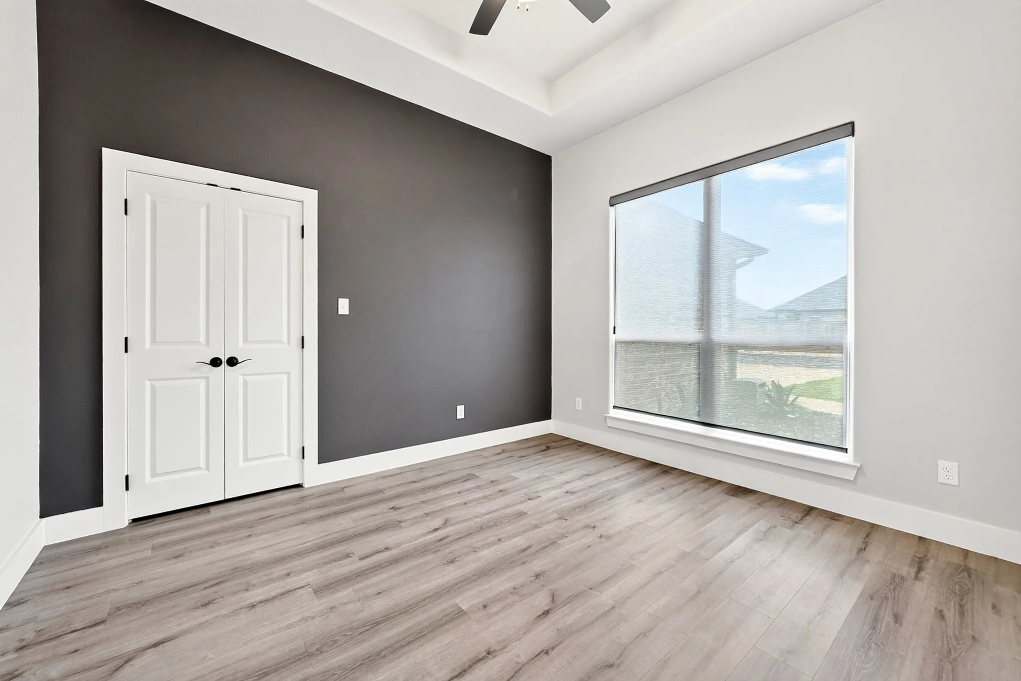 Spacious room featuring wood-finish flooring, a tray ceiling, and a ceiling fan