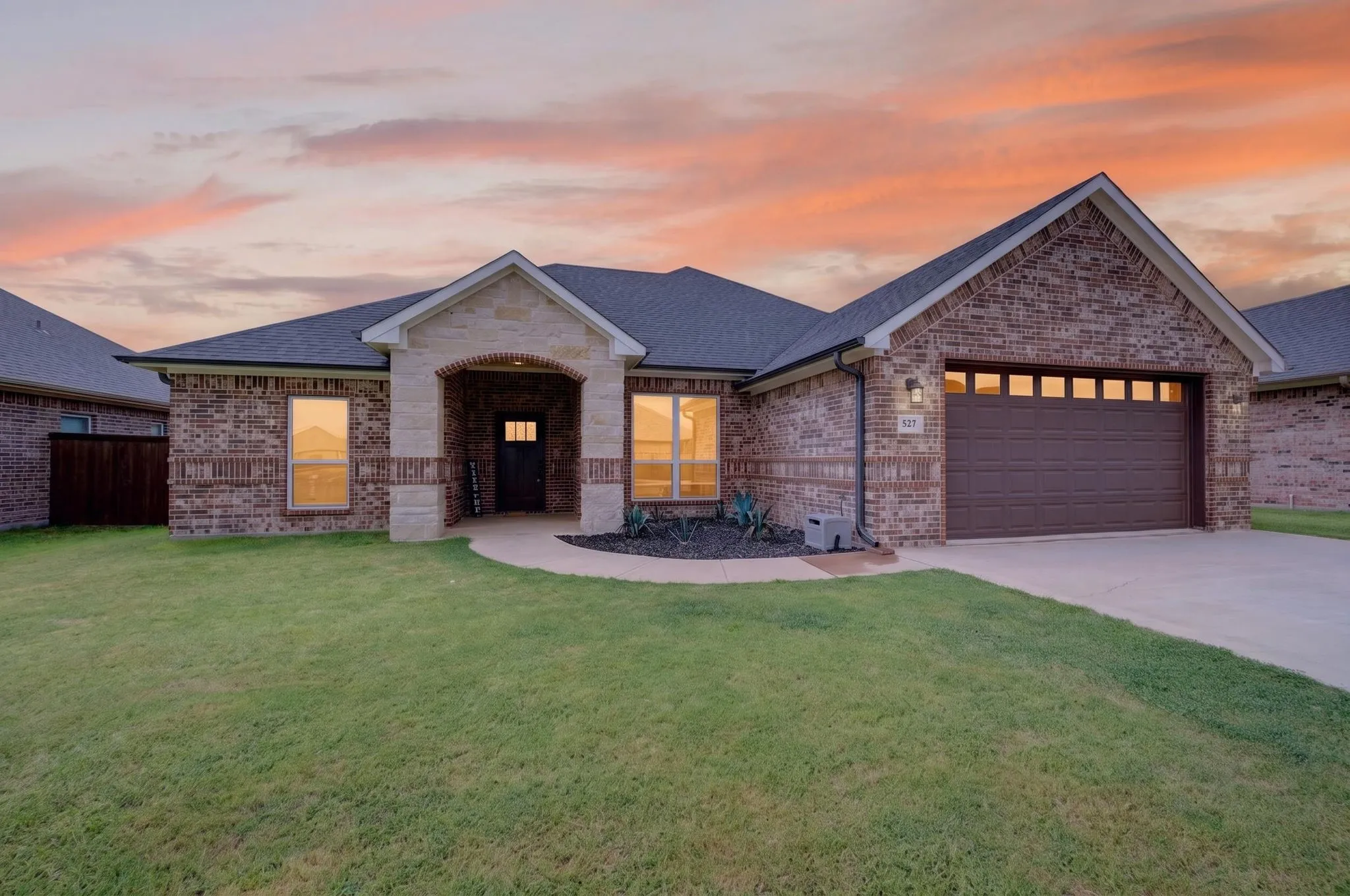 Brick and stone exterior featuring an arched entryway, a dark-paneled garage door with upper window inserts, a concrete driveway, and a front lawn with established landscaping