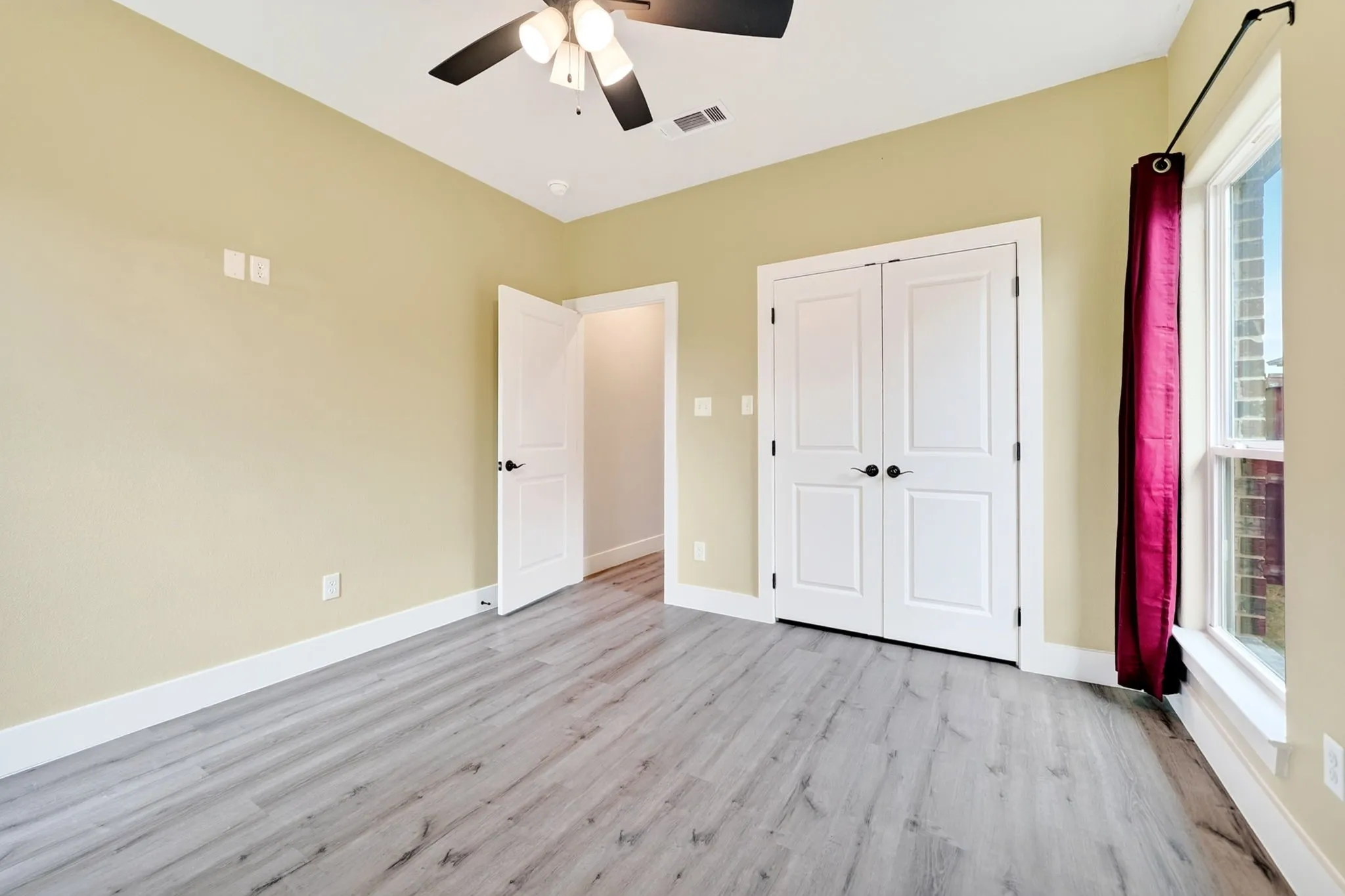 Spacious room featuring wood-finish flooring, light-toned walls, and white baseboards