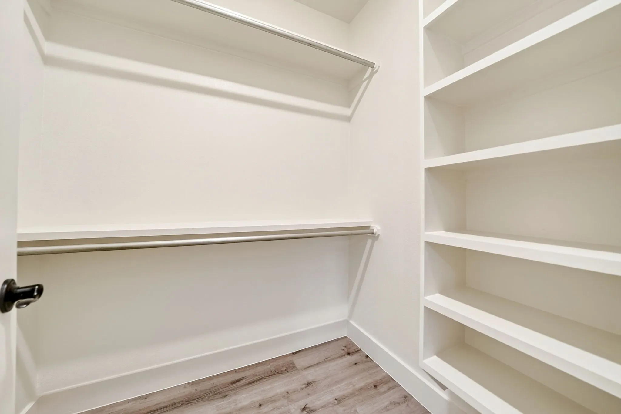 Built-in storage closet featuring multiple open shelving units, two clothing rods, white painted walls, and wood-finish flooring