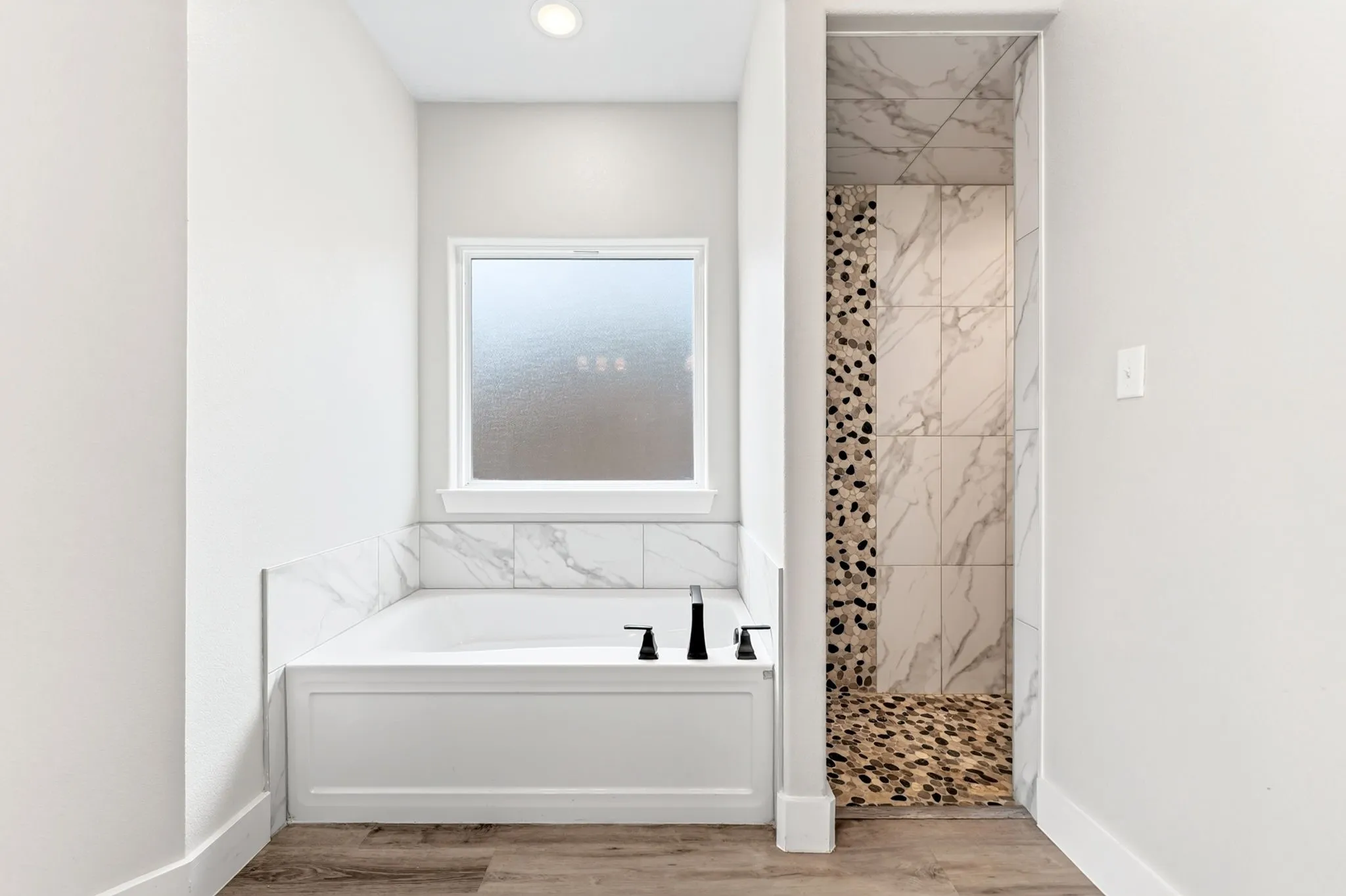 Bathroom featuring a built-in tub with a matte black faucet, surrounded by marble-style tiling