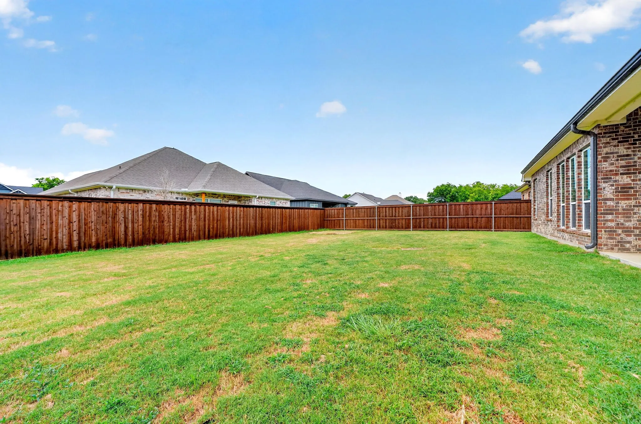 Expansive backyard featuring a wood privacy fence, green lawn, and a brick exterior with multiple windows