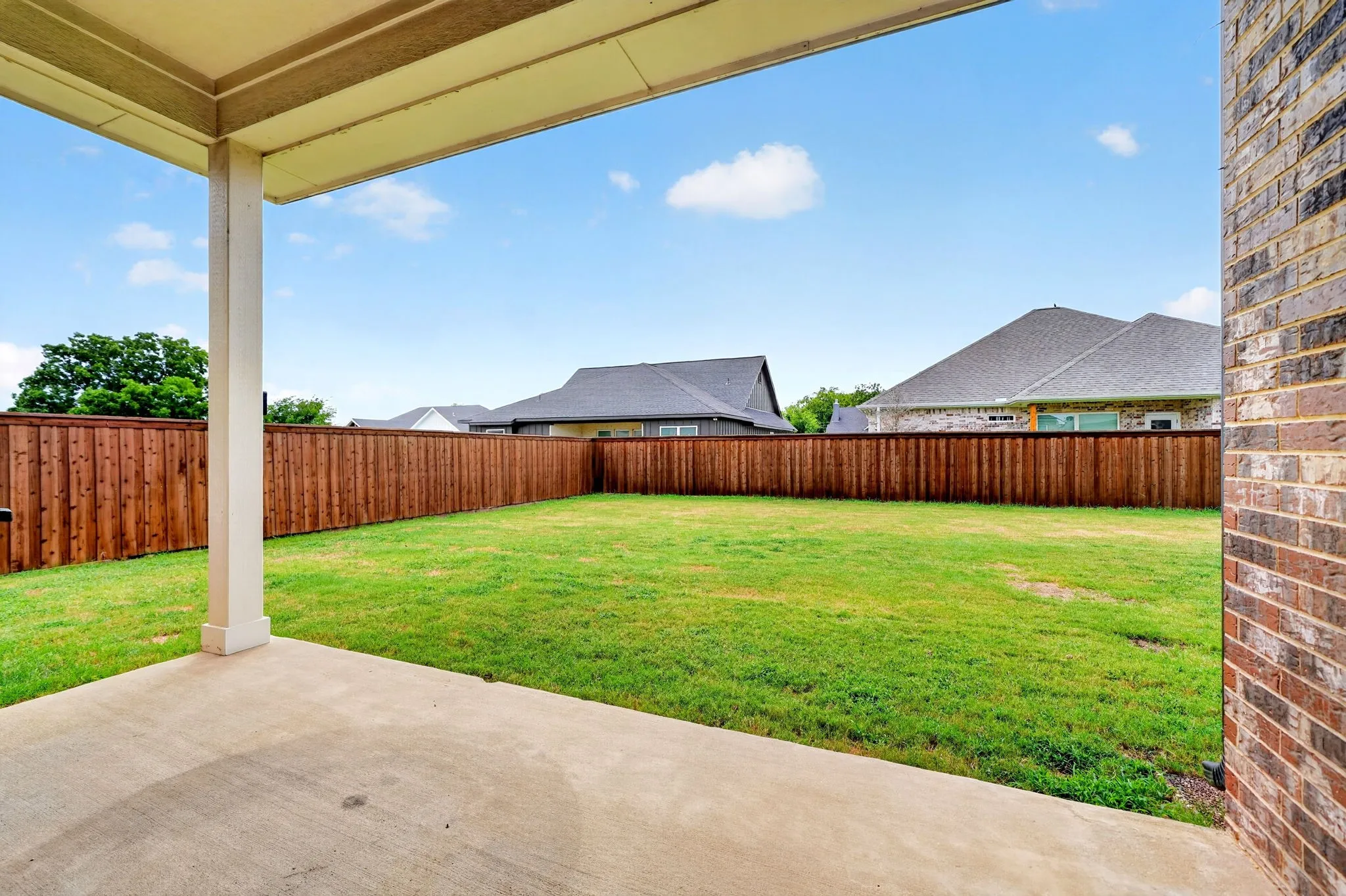 Expansive backyard featuring a covered concrete patio, wood privacy fence, and verdant lawn