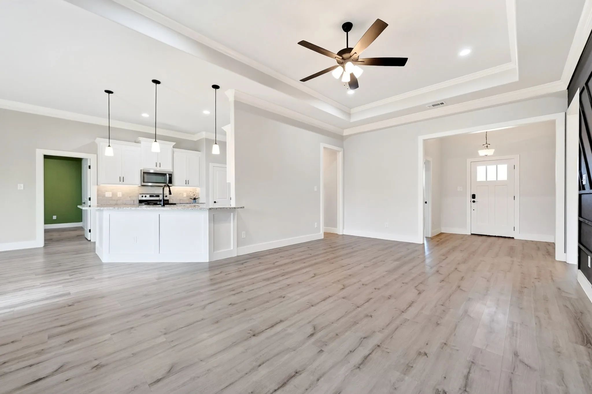 Spacious open-concept interior featuring light wood-finish flooring, a tray ceiling with a ceiling fan, and recessed lighting