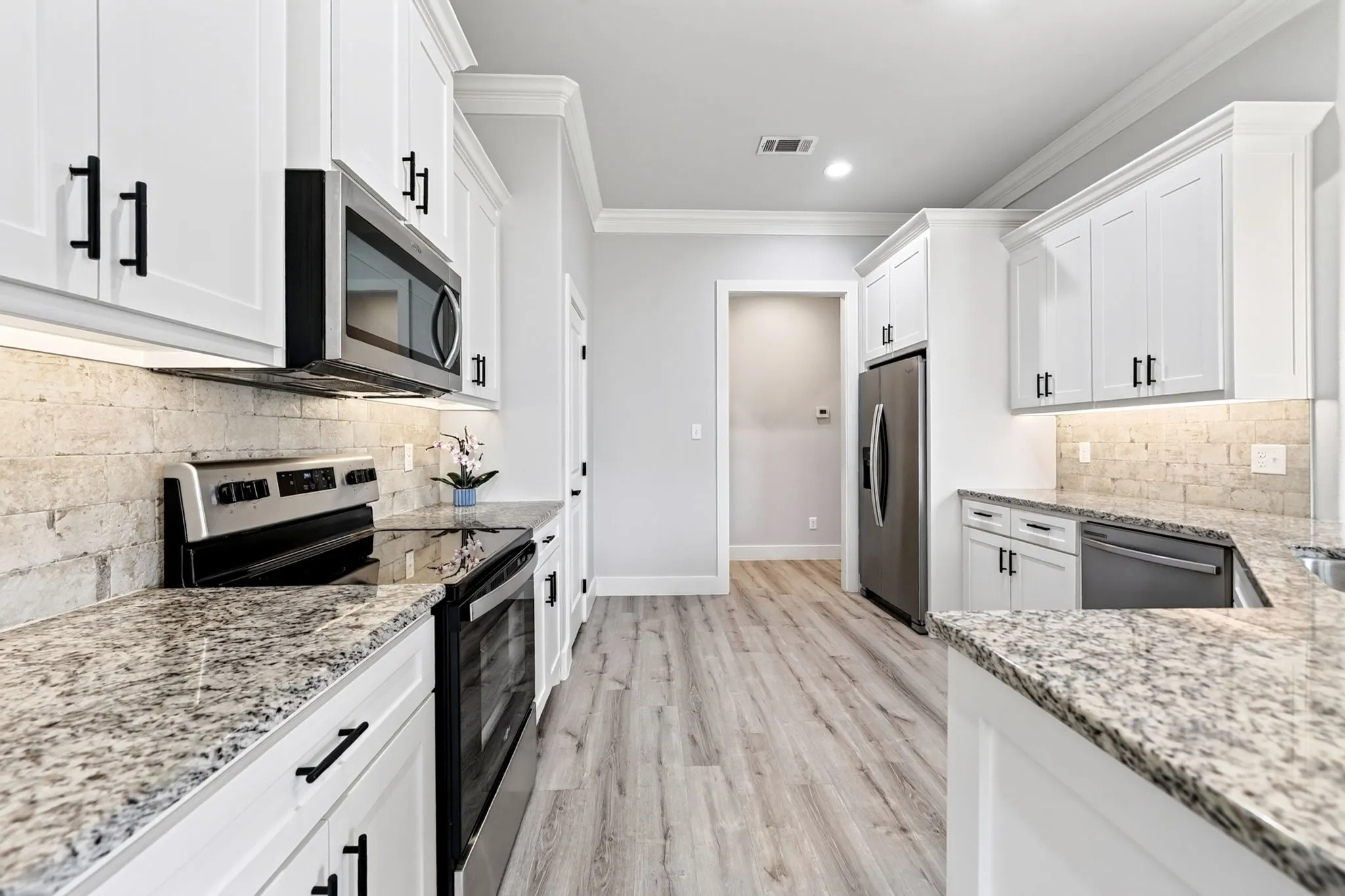Contemporary kitchen featuring white cabinetry with matte black hardware, stone-finish countertops, stainless steel appliances, a light-toned tile backsplash, and wood-finish flooring