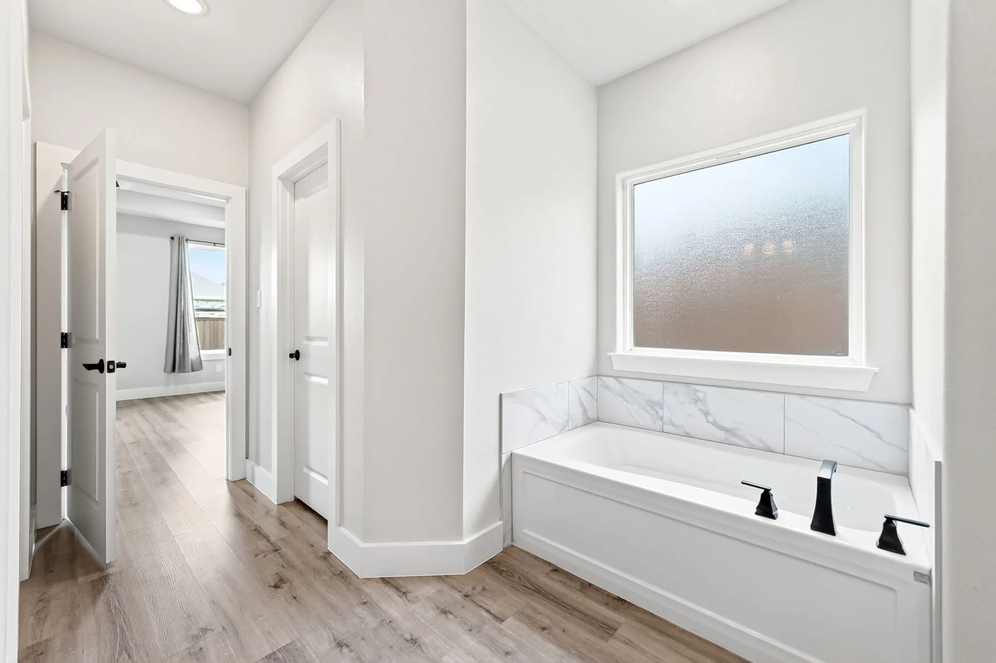 Soaking tub with white paneling and a white marble-patterned tile surround