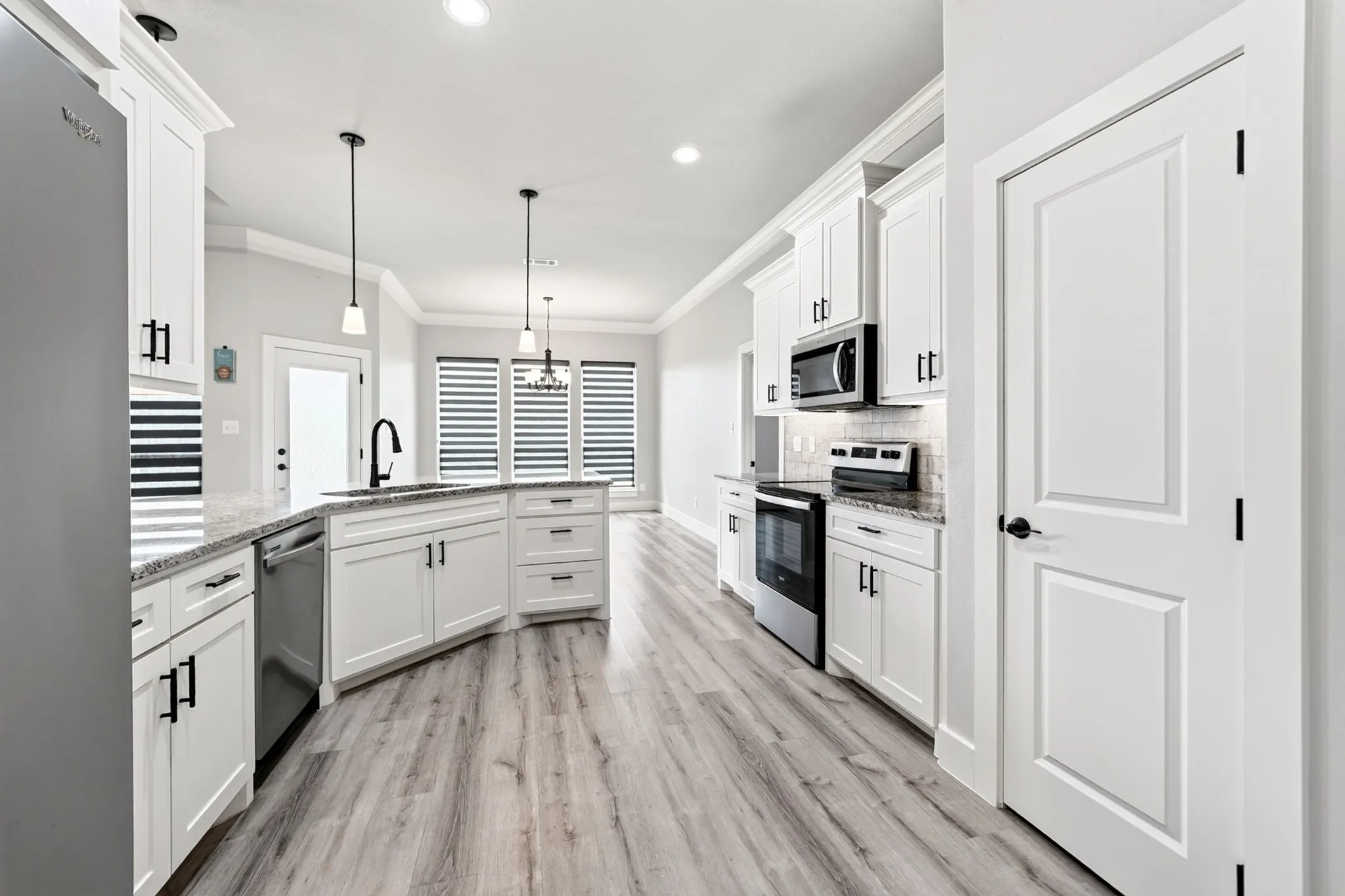 Spacious kitchen featuring an island with a built-in sink and faucet, white shaker cabinetry, granite countertops, and wood-finish flooring