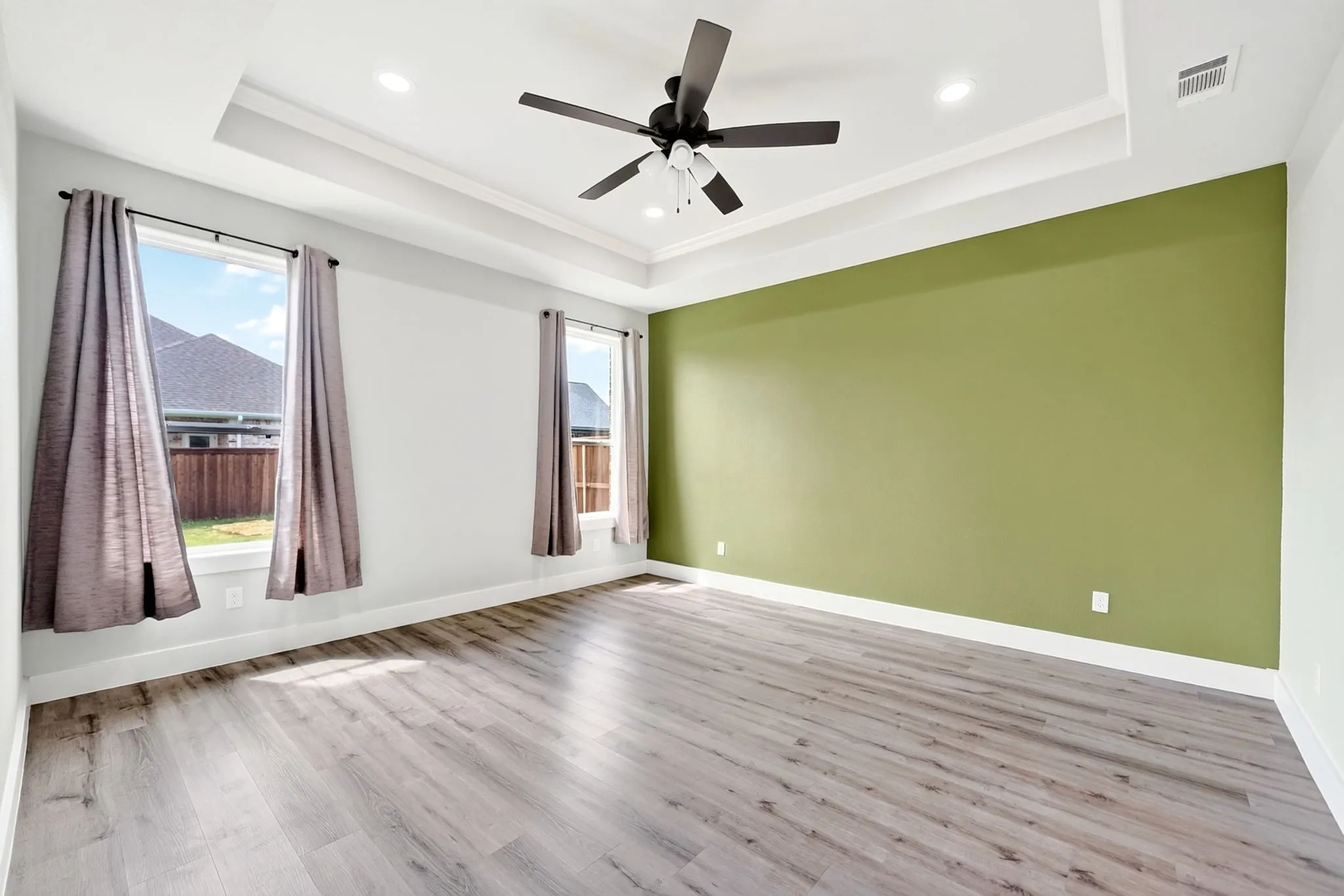 Spacious room featuring wood-finish flooring, a tray ceiling with recessed lighting, an overhead ceiling fan, and a prominent accent wall