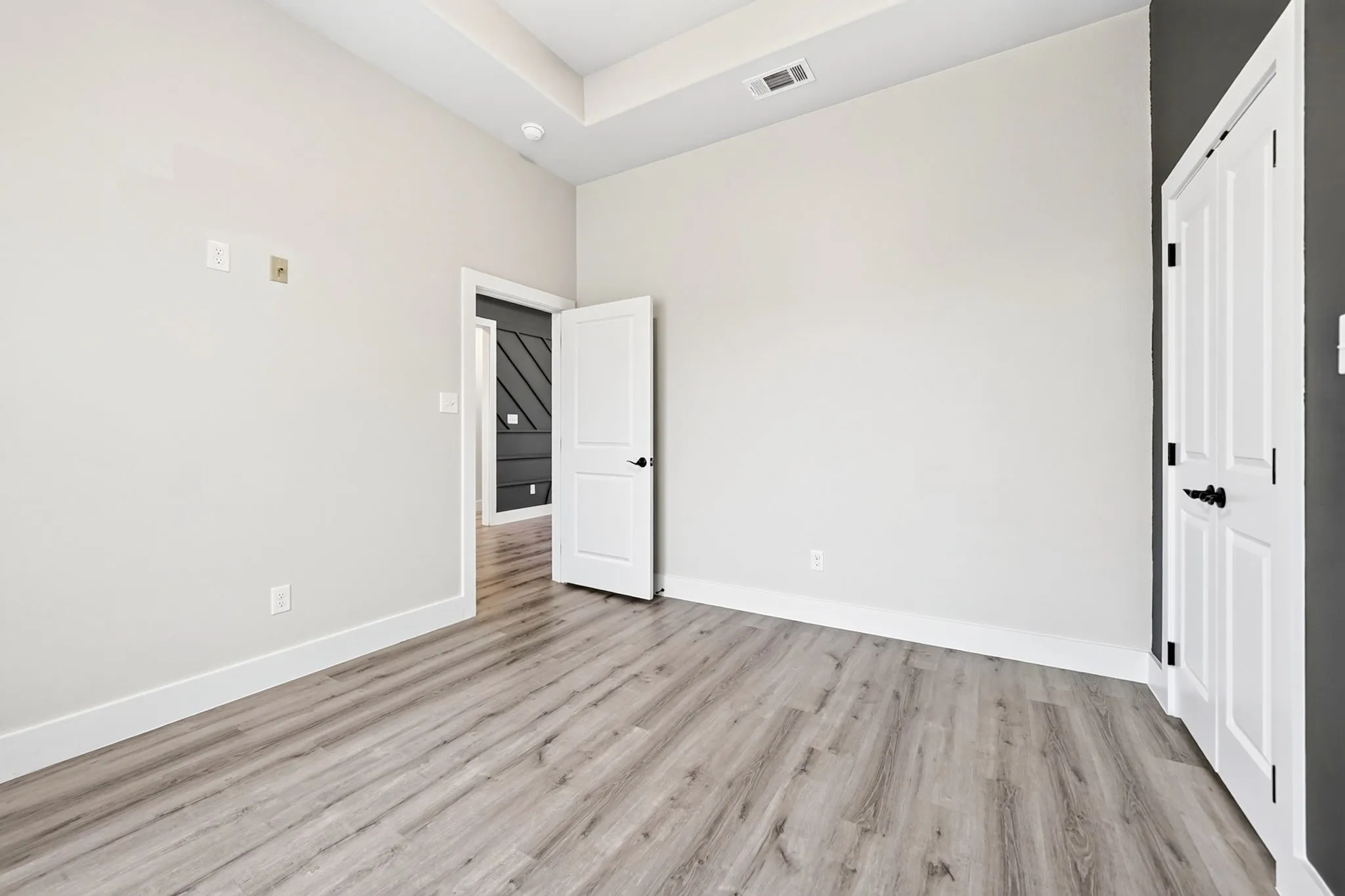 Spacious room featuring wood-finish flooring, white baseboards, and a tray ceiling