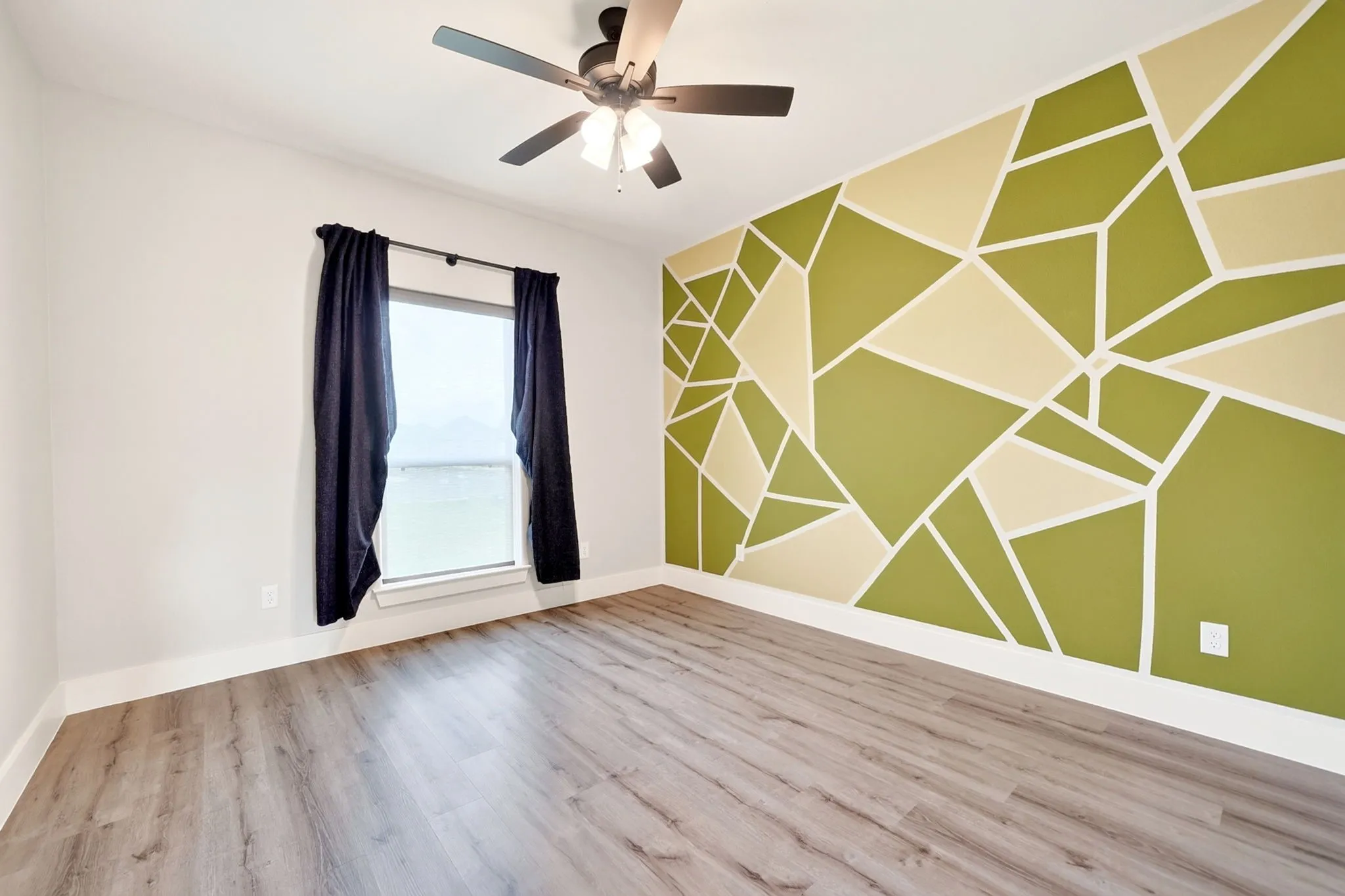 Room featuring wood-finish flooring, a contemporary accent wall with geometric design, and a ceiling fan with integrated lighting