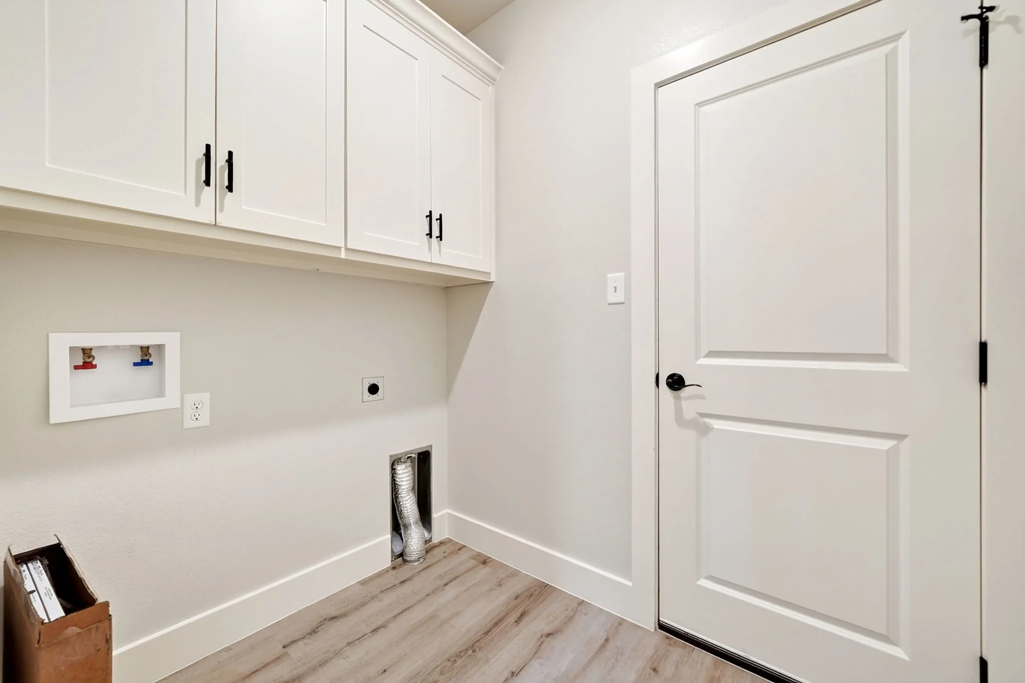 Laundry area featuring upper cabinetry with black hardware, wood-finish flooring, and a solid core door