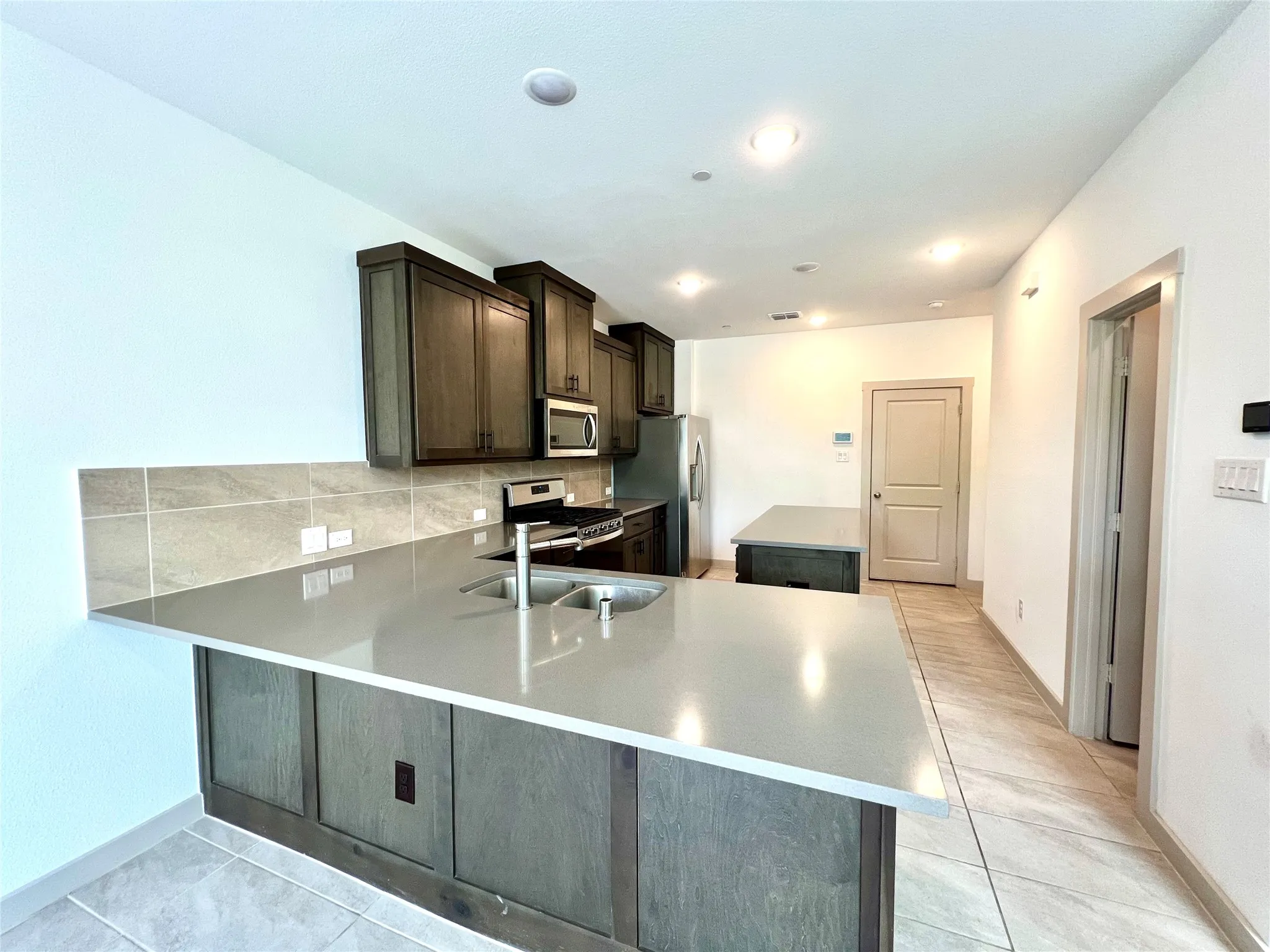 Kitchen with appliances with stainless steel finishes, tasteful backsplash, kitchen peninsula, sink, and dark brown cabinetry