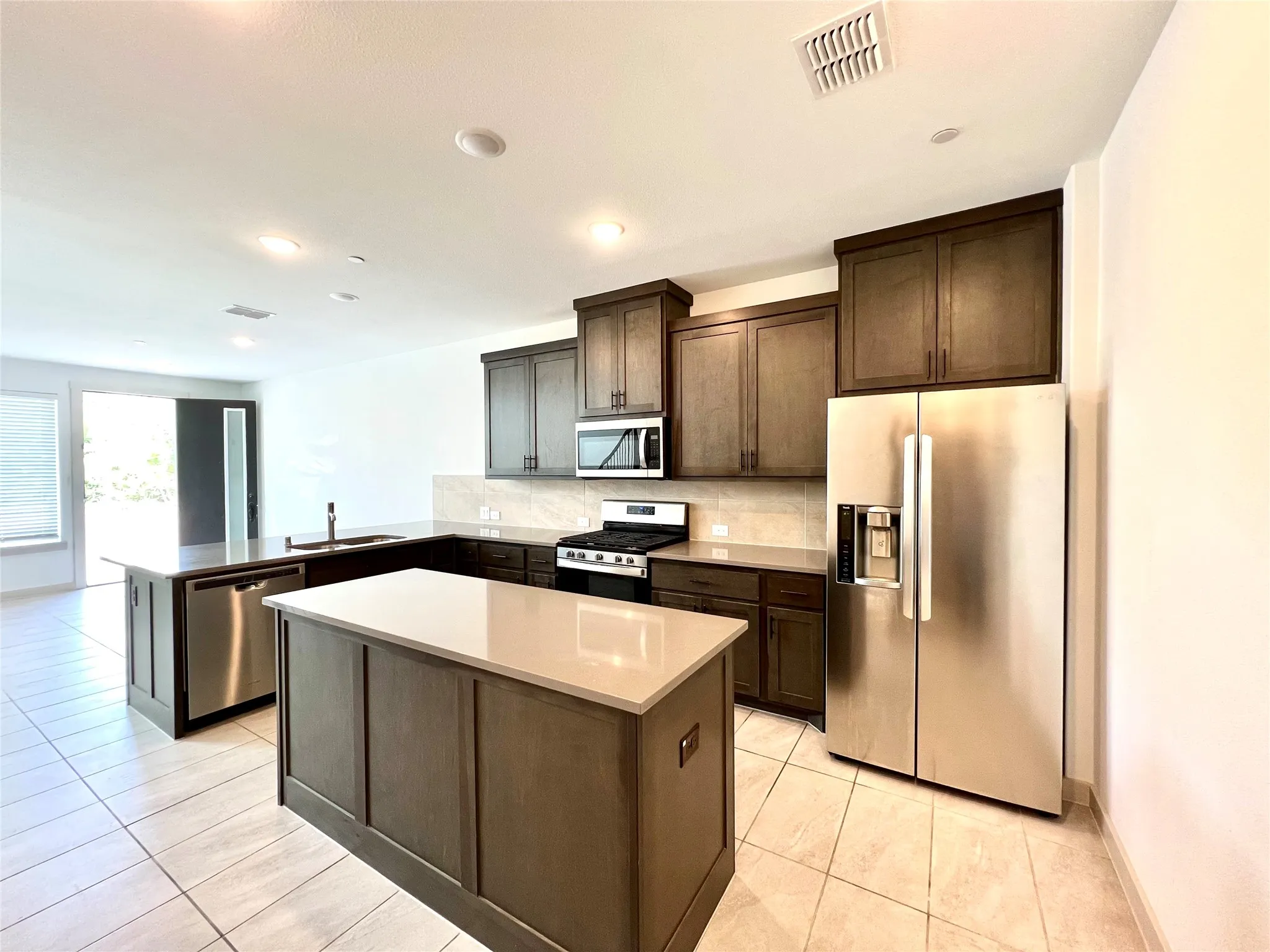Kitchen with stainless steel appliances, kitchen peninsula, sink, decorative backsplash, and a kitchen island