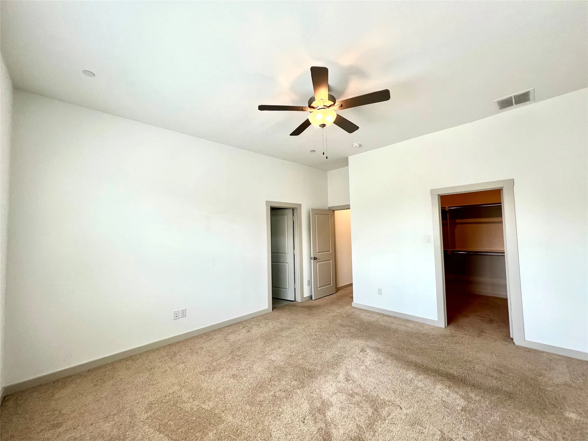 Unfurnished bedroom featuring light colored carpet, a spacious closet, ceiling fan, and a closet