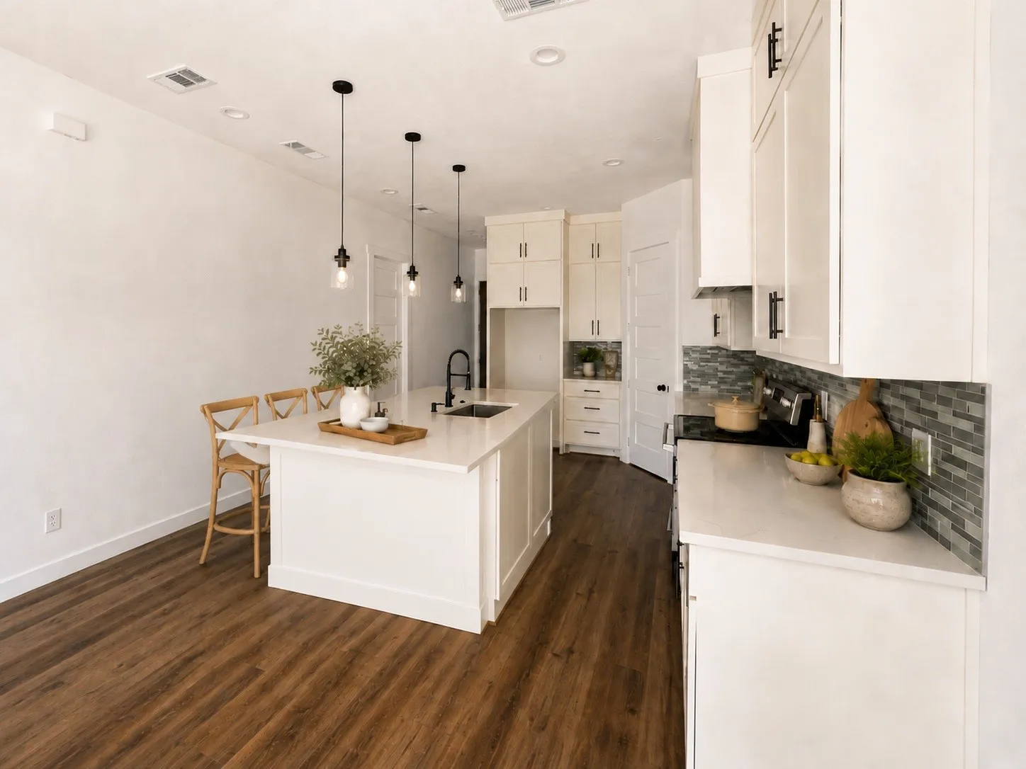 Kitchen featuring wood-finish flooring, white cabinetry with dark hardware, a white kitchen island with an integrated sink, white countertops, and a tiled backsplash