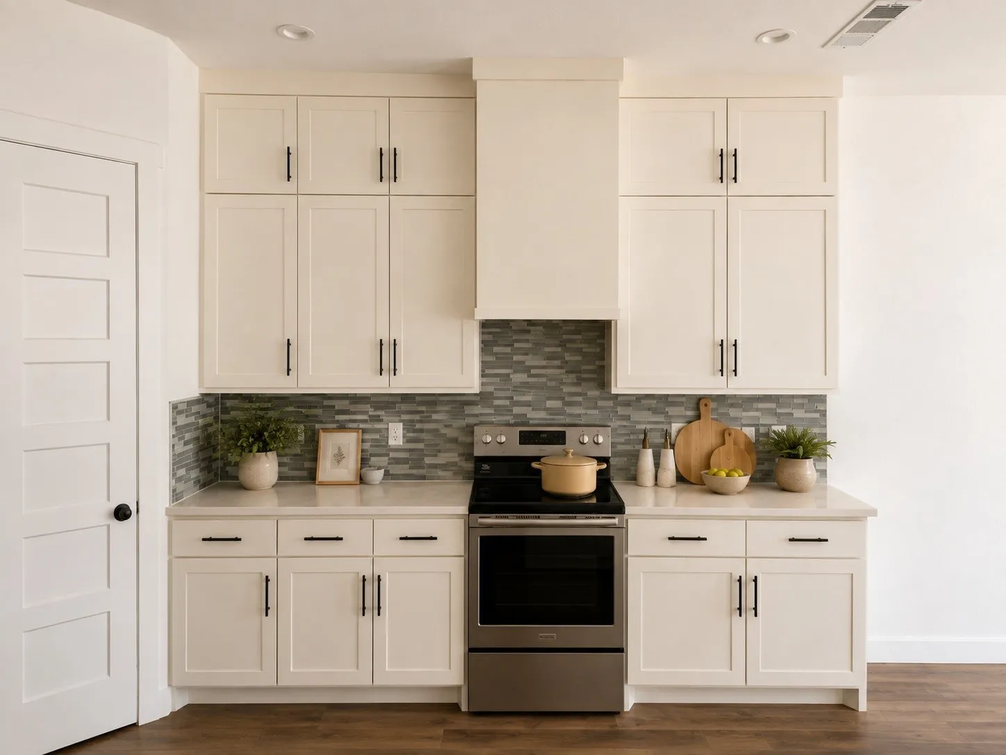 White shaker cabinetry with matte black hardware, mosaic tile backsplash, stainless steel range, and light-toned countertops