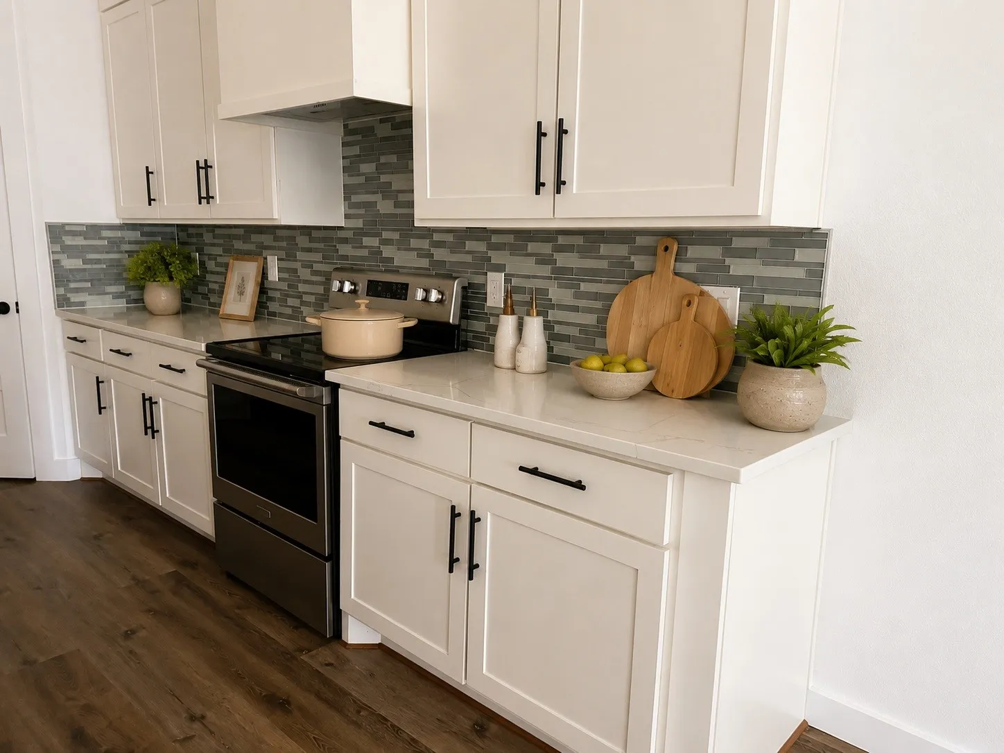 White shaker cabinetry, light-toned countertops, full-height mosaic tile backsplash, stainless steel range, and wood-finish flooring