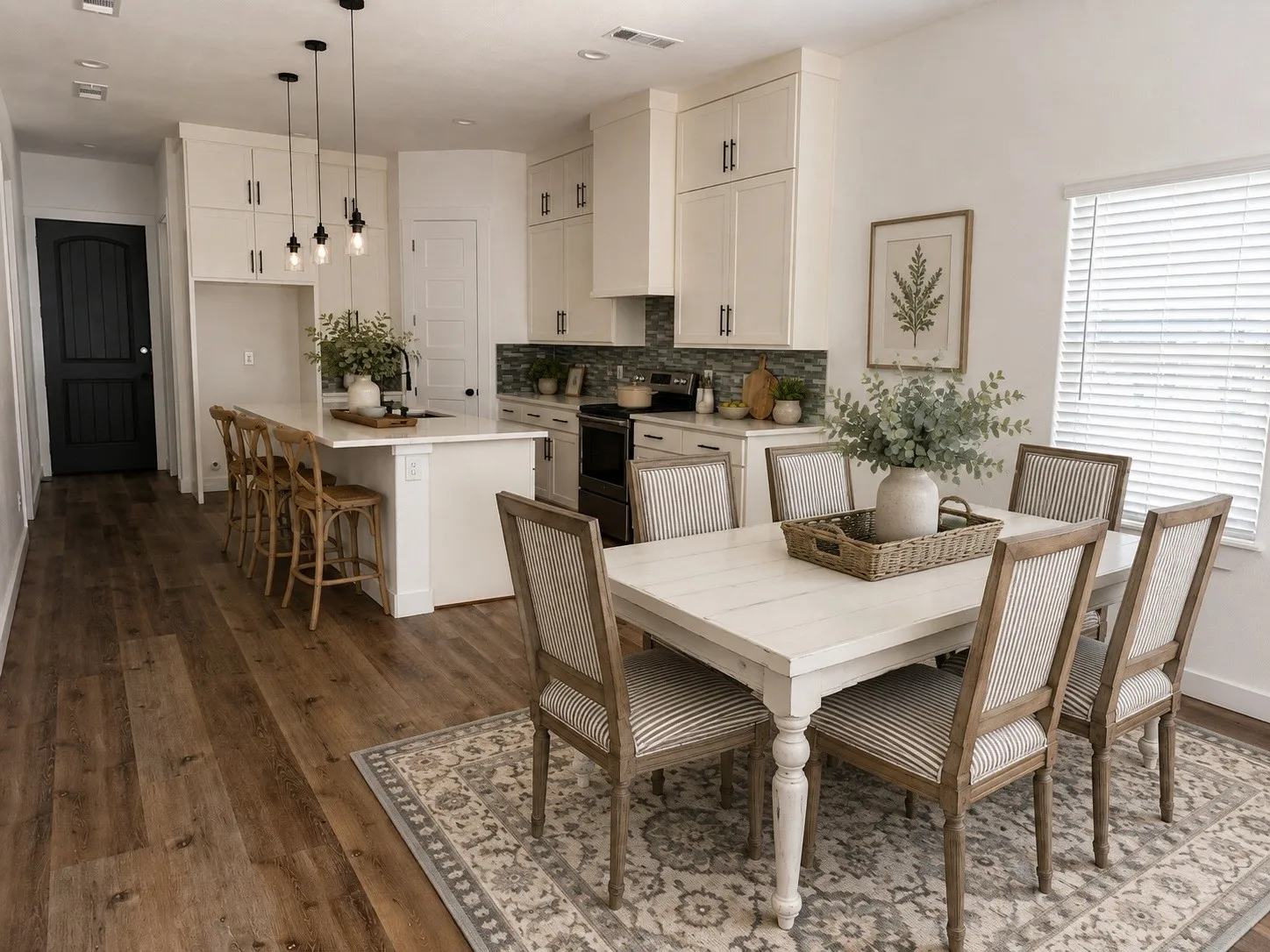 Open-concept living area featuring wood-finish flooring, a kitchen island with seating, pendant lighting, white cabinetry with dark hardware, and a tiled kitchen backsplash