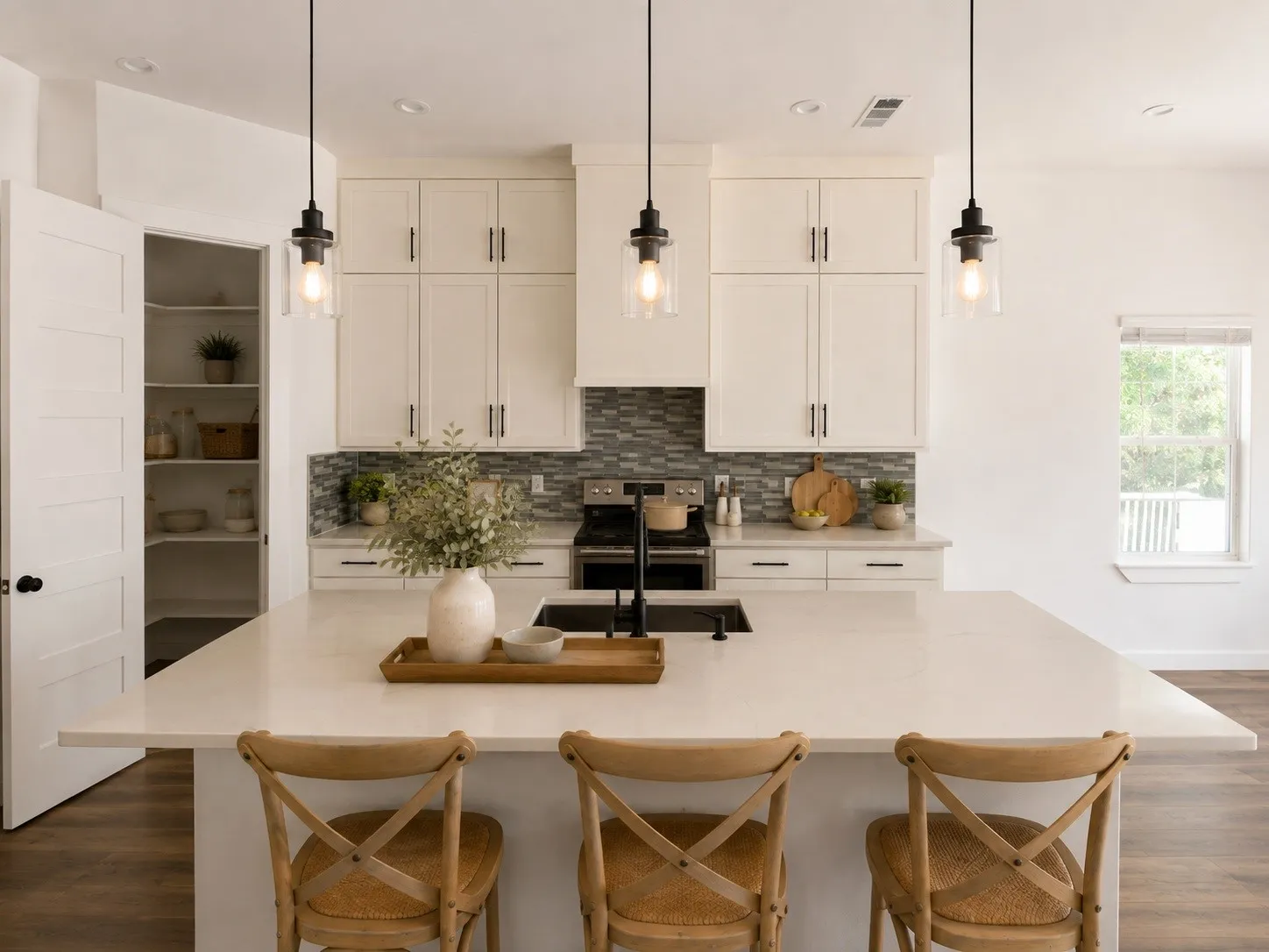 Spacious kitchen island with seating, white shaker cabinetry, mosaic tile backsplash, black appliance suite, and walk-in pantry with built-in shelving