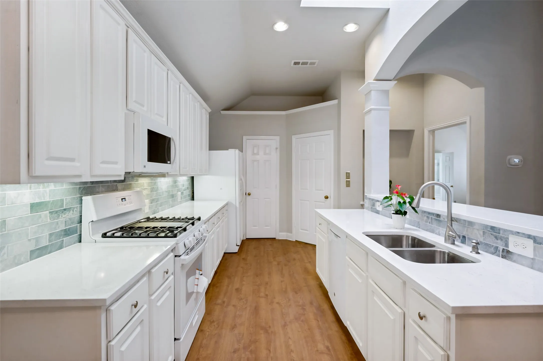 Bright kitchen featuring white cabinetry, gas burning stove, light counter tops, wood-finish flooring, a stainless steel double basin sink with a high-arc faucet, and an arched architectural detail
