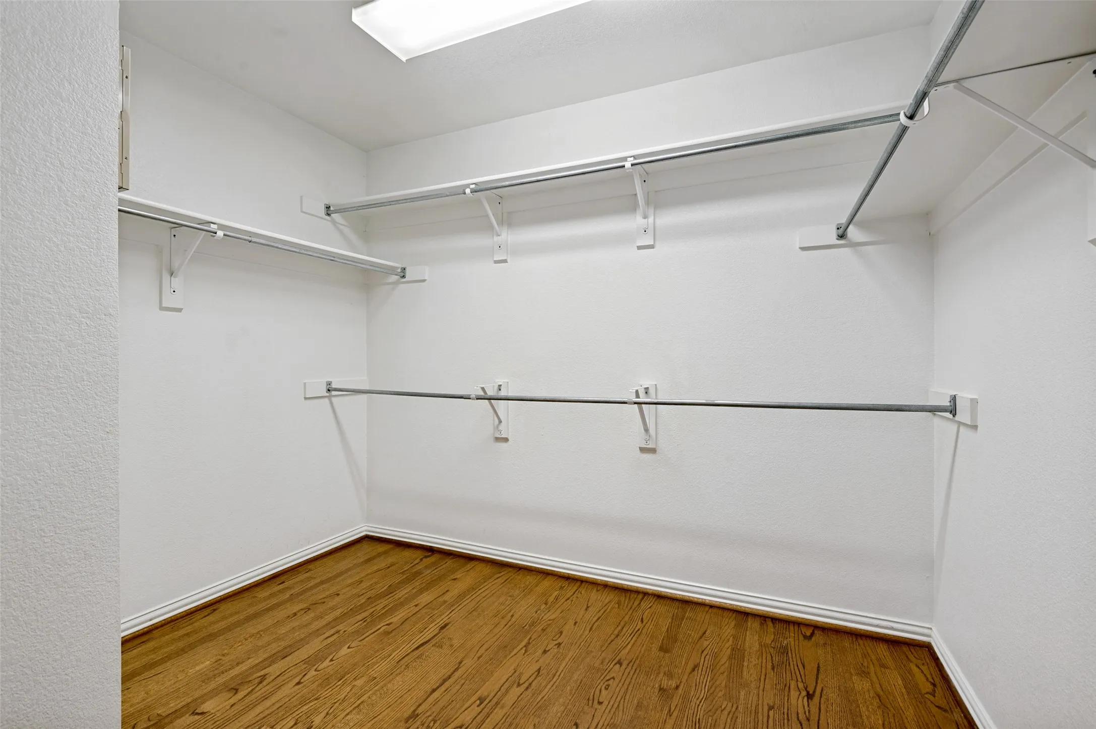 Spacious walk-in closet featuring wood-finish flooring and multiple shelving and hanging rods