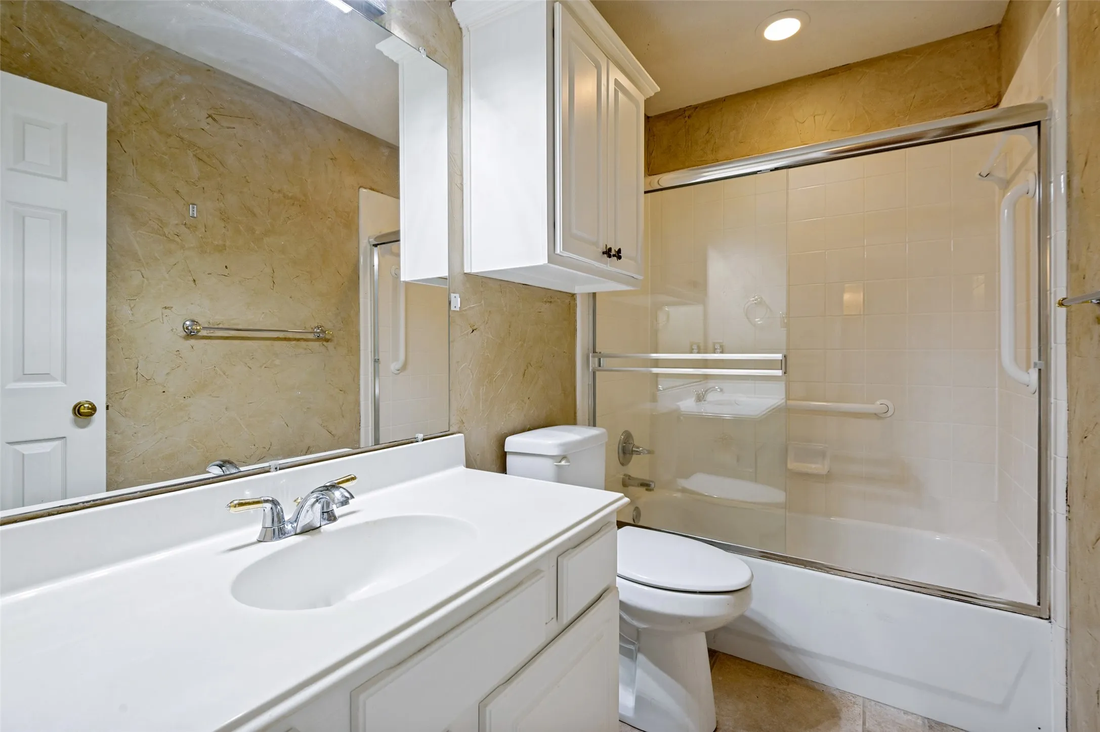 Full bathroom featuring a white vanity with integrated sink, chrome faucet, and overhead cabinetry