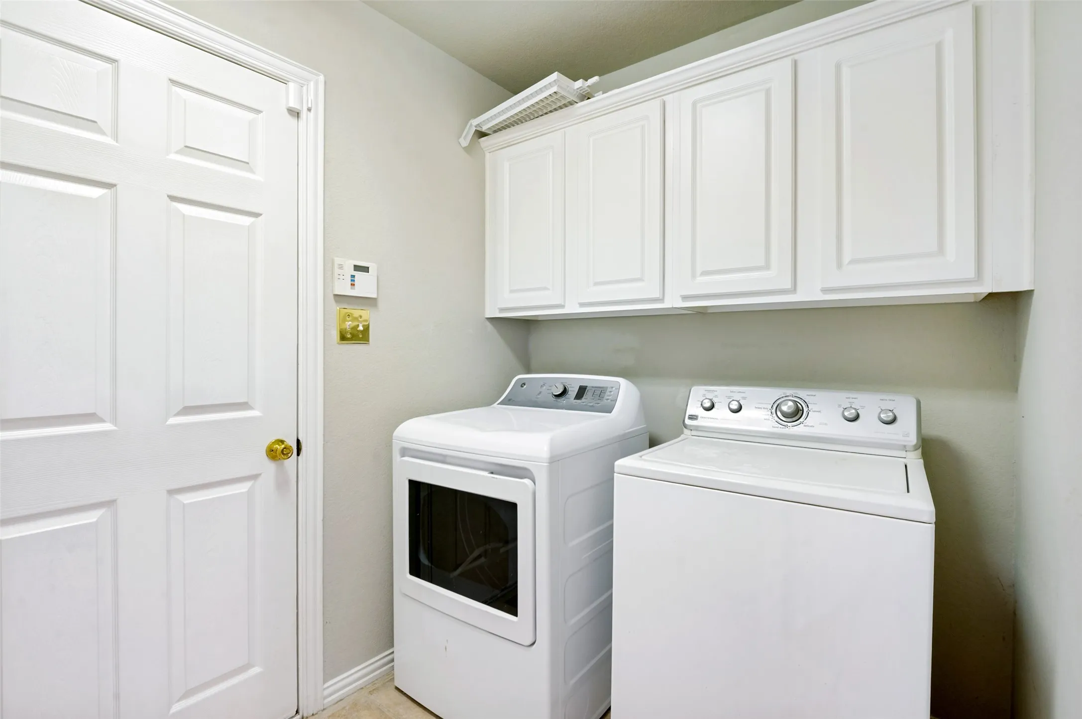Laundry area featuring overhead white paneled cabinetry, light neutral wall paint, and light-toned flooring
