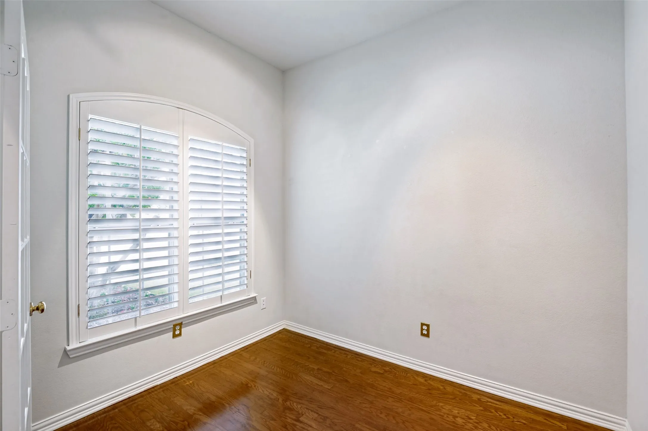 Room featuring an arched window with plantation shutters, wood-finish flooring, and white baseboards
