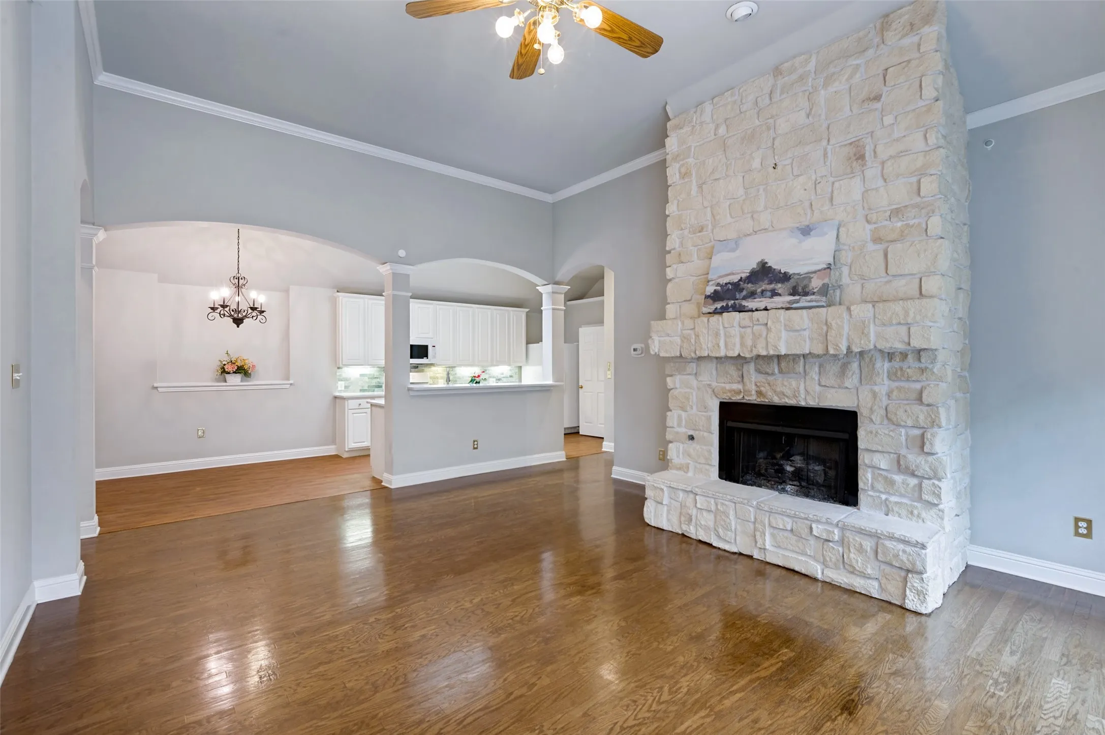 Stone-faced fireplace with a black hearth and mantle, wood-finish flooring, crown molding, and arched doorways