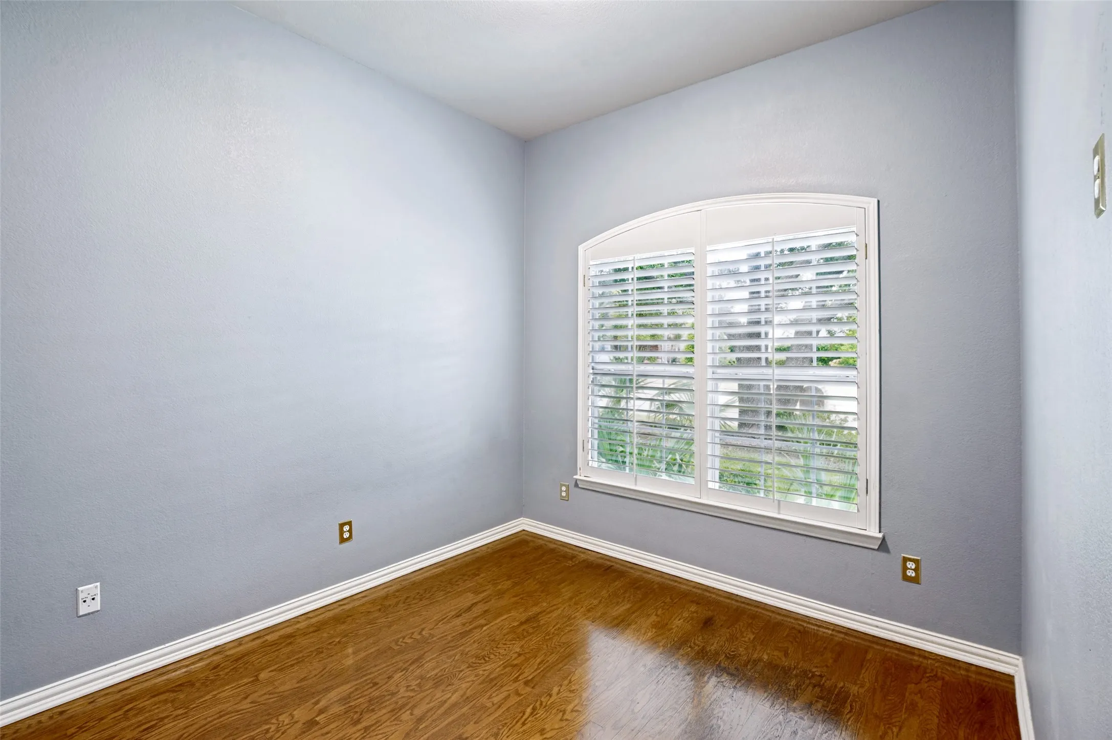 Room featuring wood-finish flooring, plantation shutters, light blue wall paint, and white baseboards