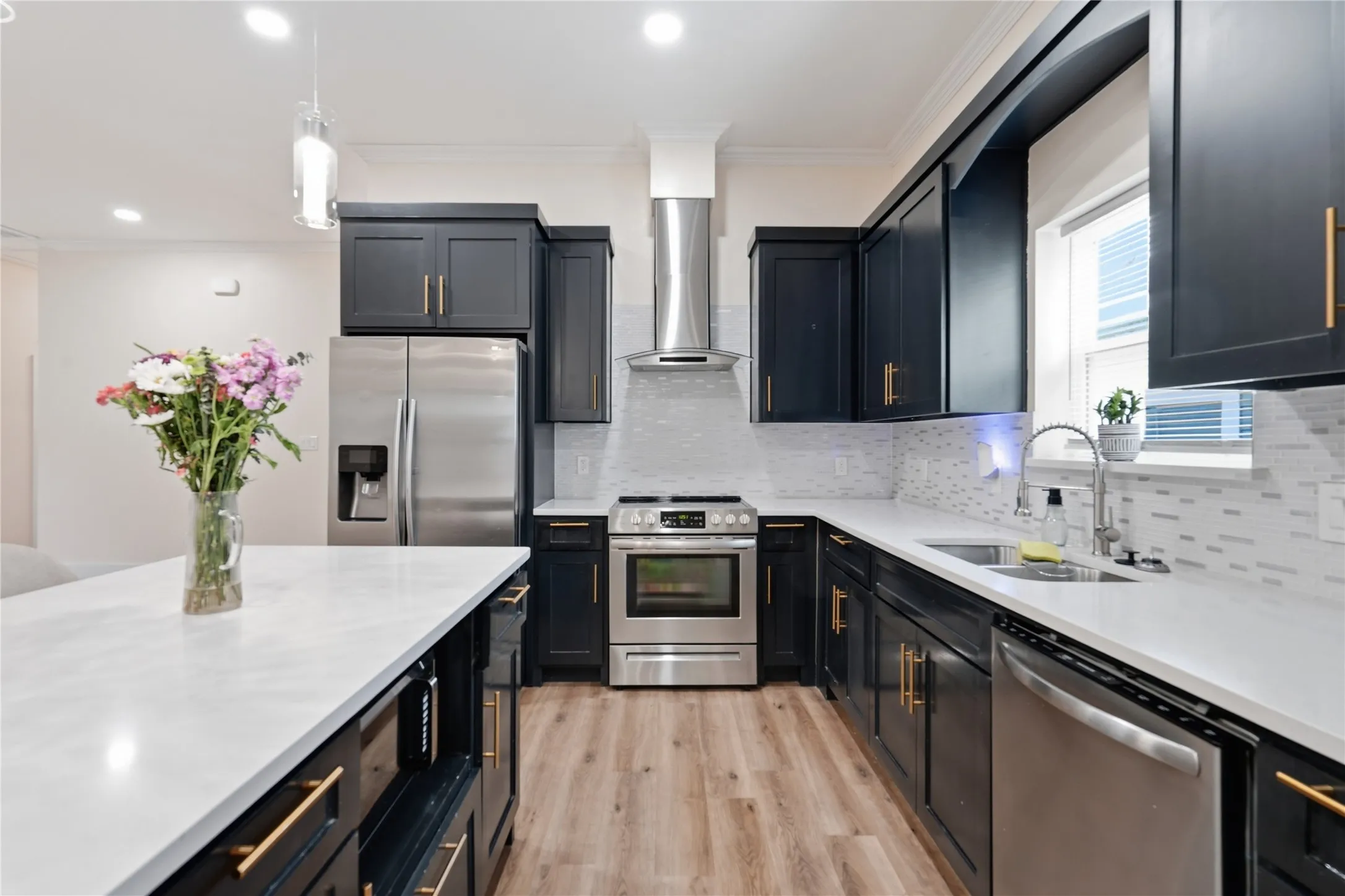 Kitchen featuring dark cabinetry with gold-tone hardware, stainless steel appliances, light countertops, a white tile backsplash, and Luxury Vinyl Flooring