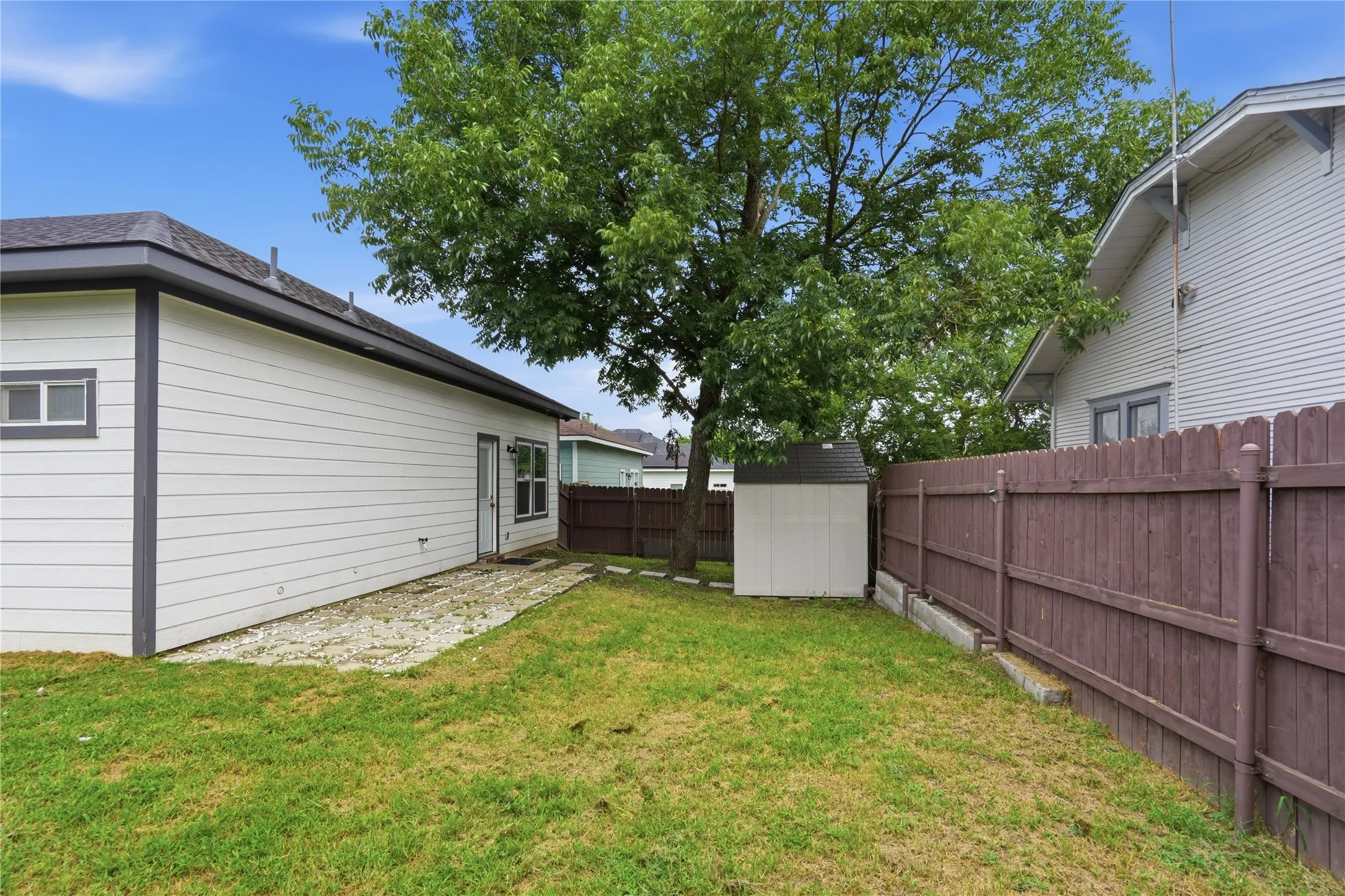 Expansive backyard featuring a green lawn, mature trees, and a privacy fence