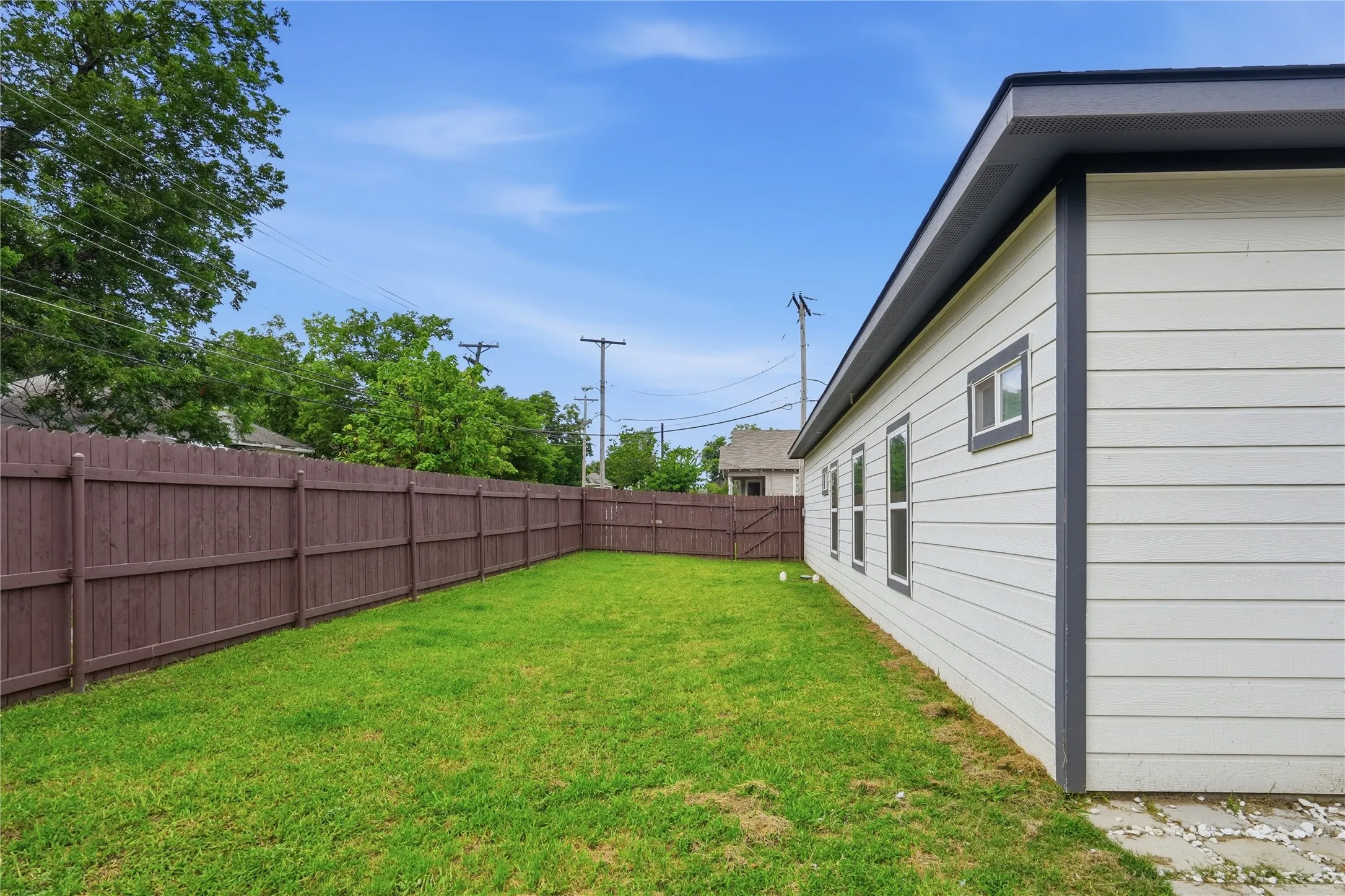 Expansive backyard featuring a manicured lawn, a full privacy fence, and a white siding exterior with dark trim