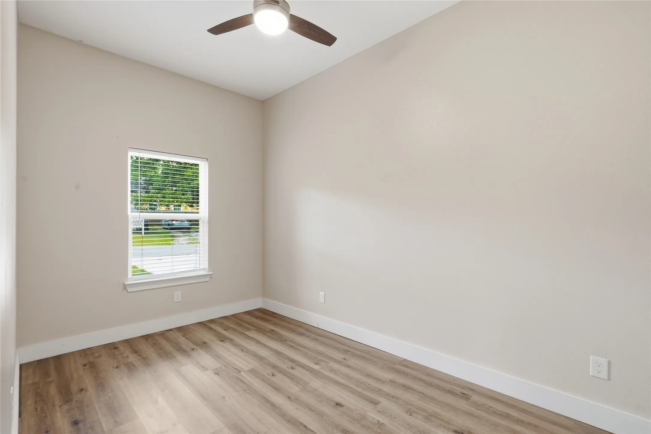 Room featuring neutral wall tones, wood-finish flooring, a contemporary ceiling fan with integrated lighting, and a single window with horizontal blinds