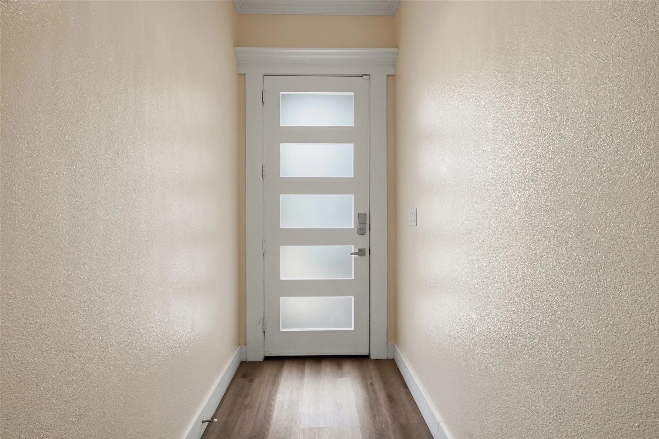 Modern entryway featuring a contemporary front door with frosted glass panels, soaring ceilings, elegant crown molding, and luxury vinyl plank flooring that creates a bright and welcoming first impression