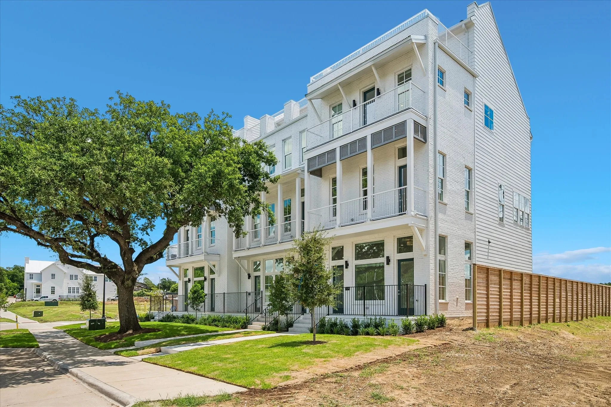 Modern townhome featuring white brick and horizontal siding, multiple balconies with black iron railings, and a horizontal slat privacy fence