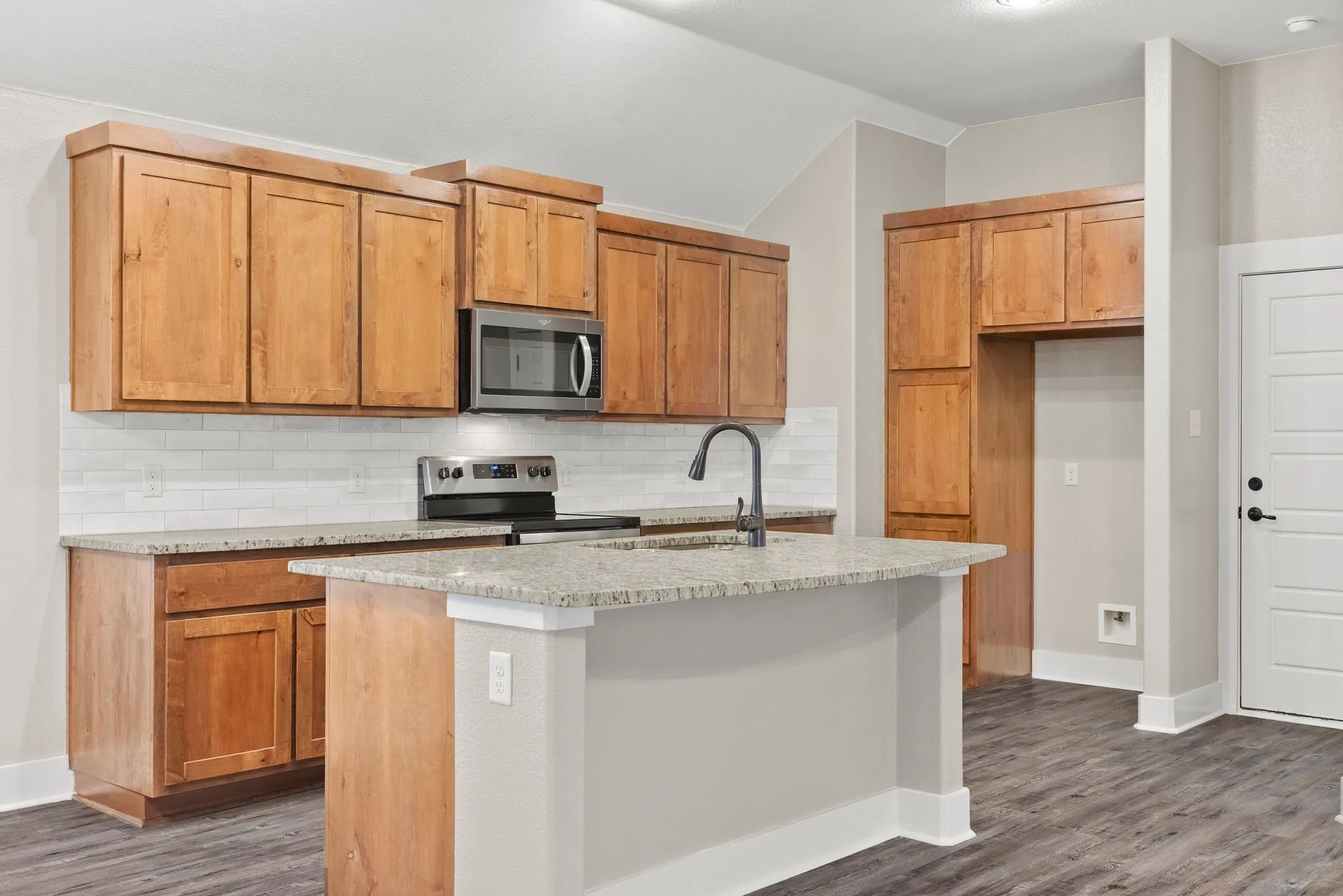 Kitchen with subway tile backsplash, stainless steel appliances, granite counters, an island with sink, and lofted ceiling