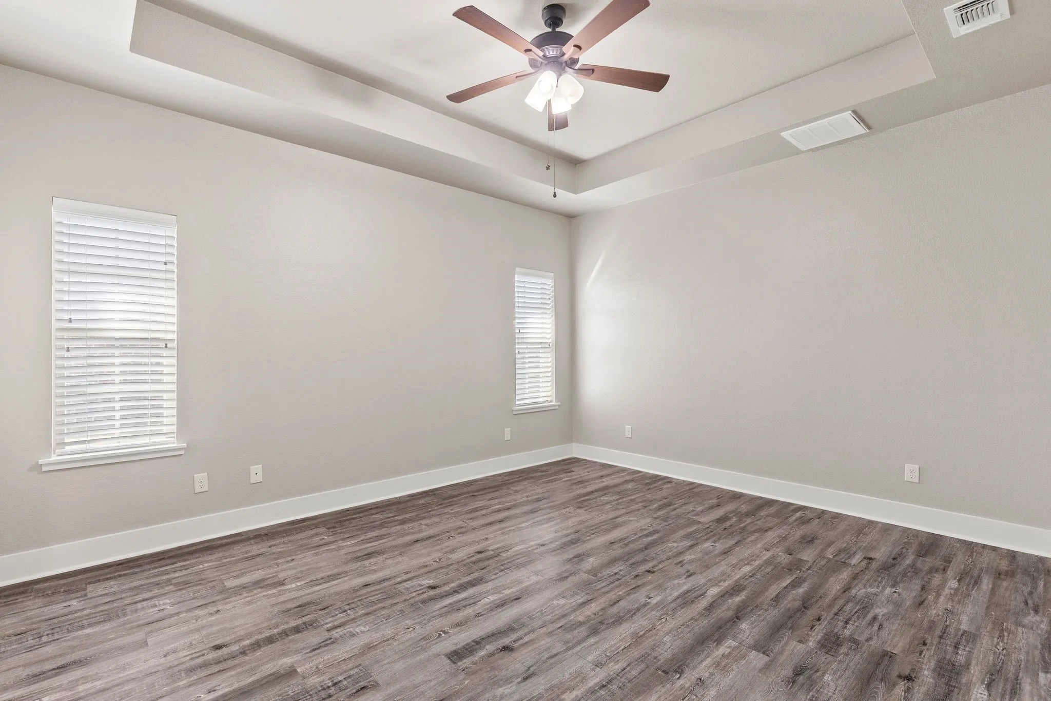 Raised ceiling, ceiling fan, and dark wood finished floors