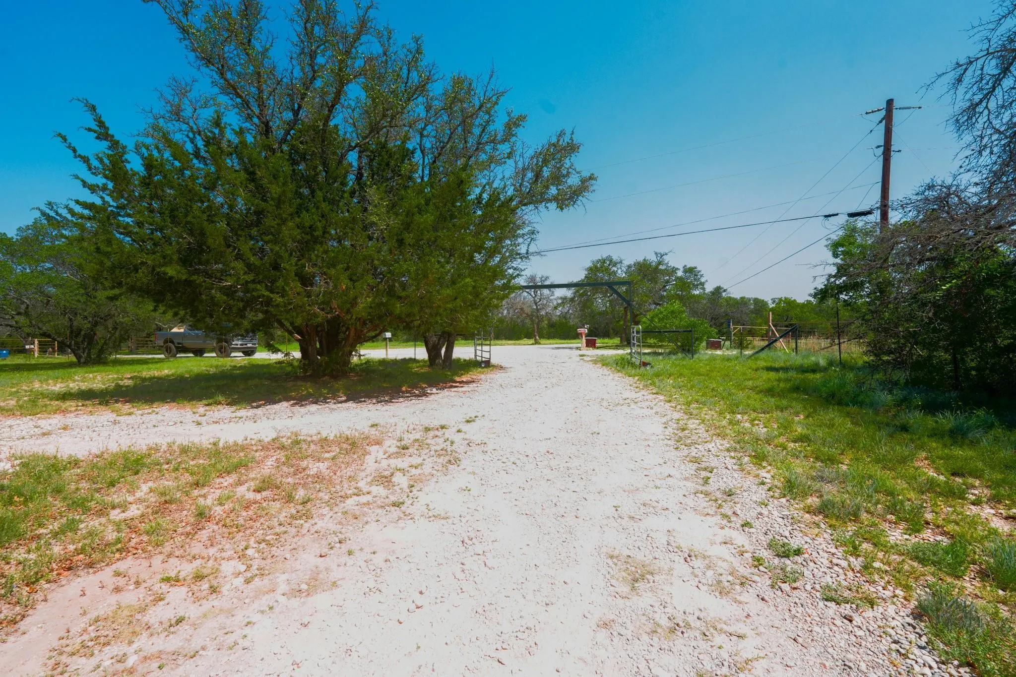 Gravel driveway opening to a gated entrance with mature trees and natural landscaping