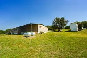 Expansive grassy landscape featuring a single-story structure with tan siding, a covered porch, and two large cylindrical tanks