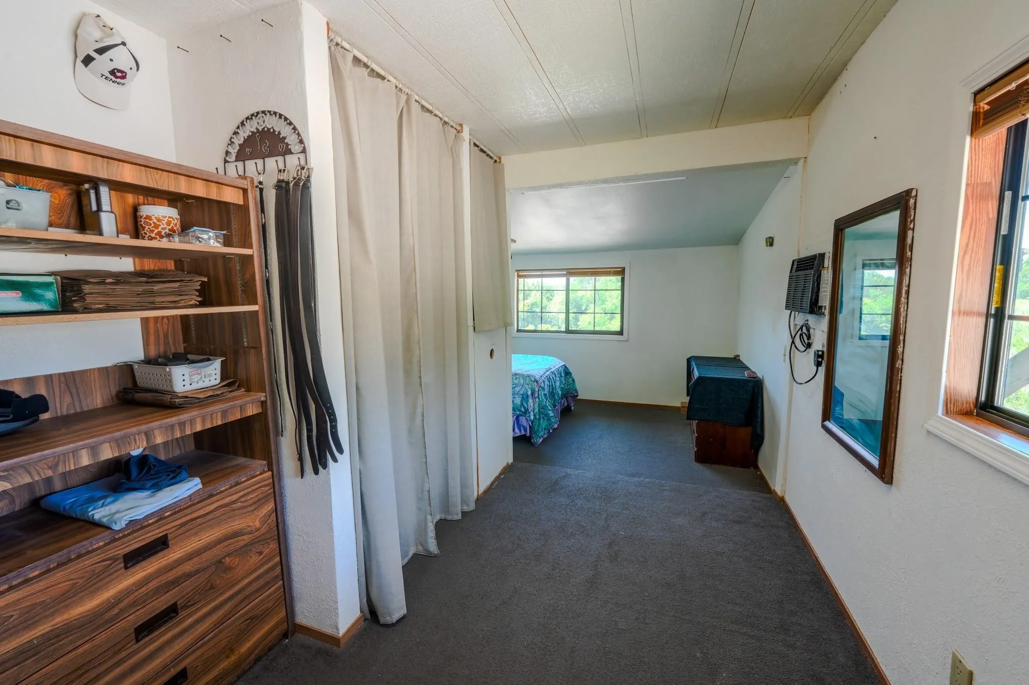Carpeted room featuring a built-in wood-finish shelving unit with integrated drawers, multiple windows, and a ceiling with exposed beams