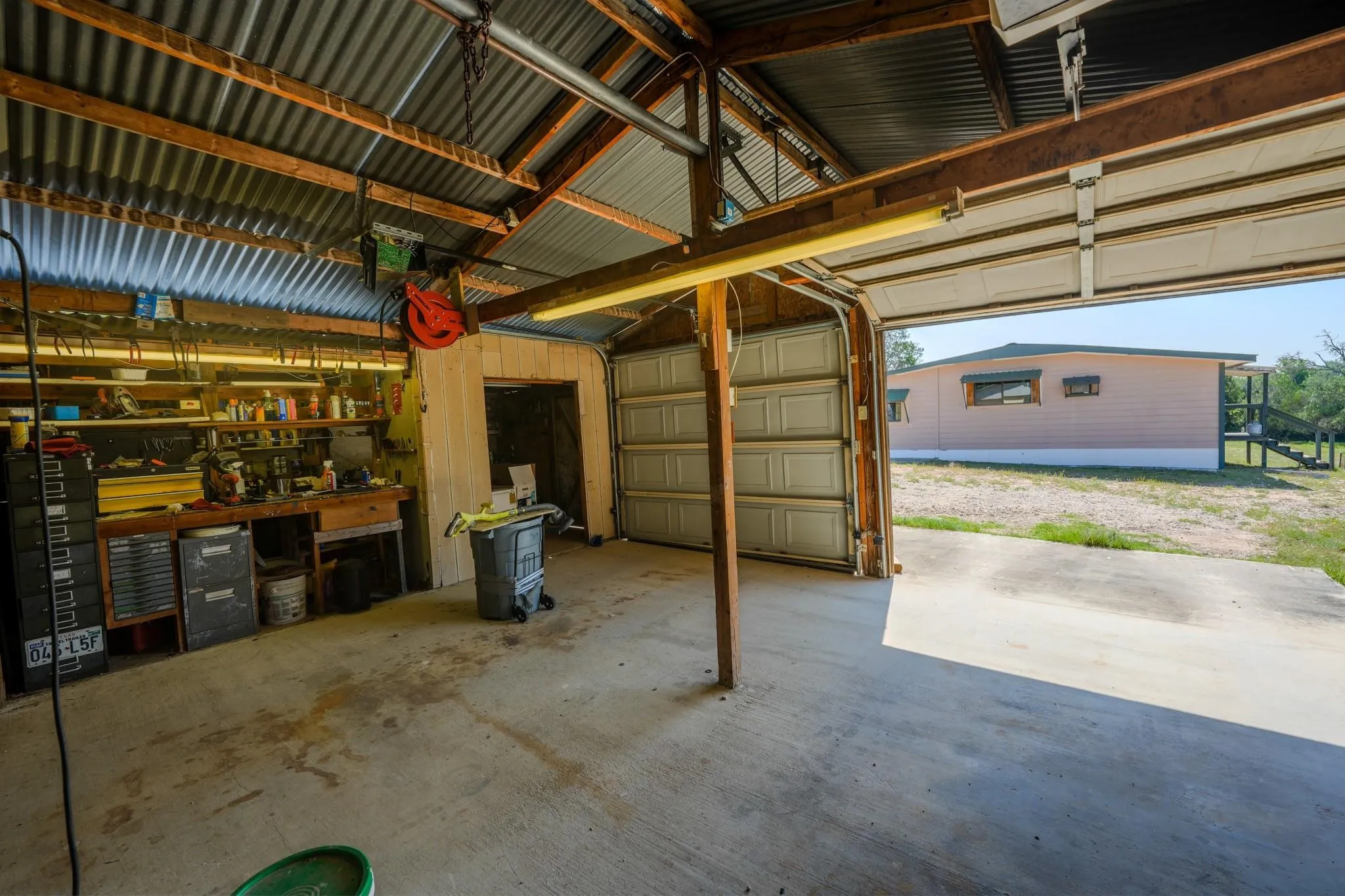 Utility garage featuring a corrugated metal ceiling, exposed wood beams, concrete flooring, and a built-in workbench