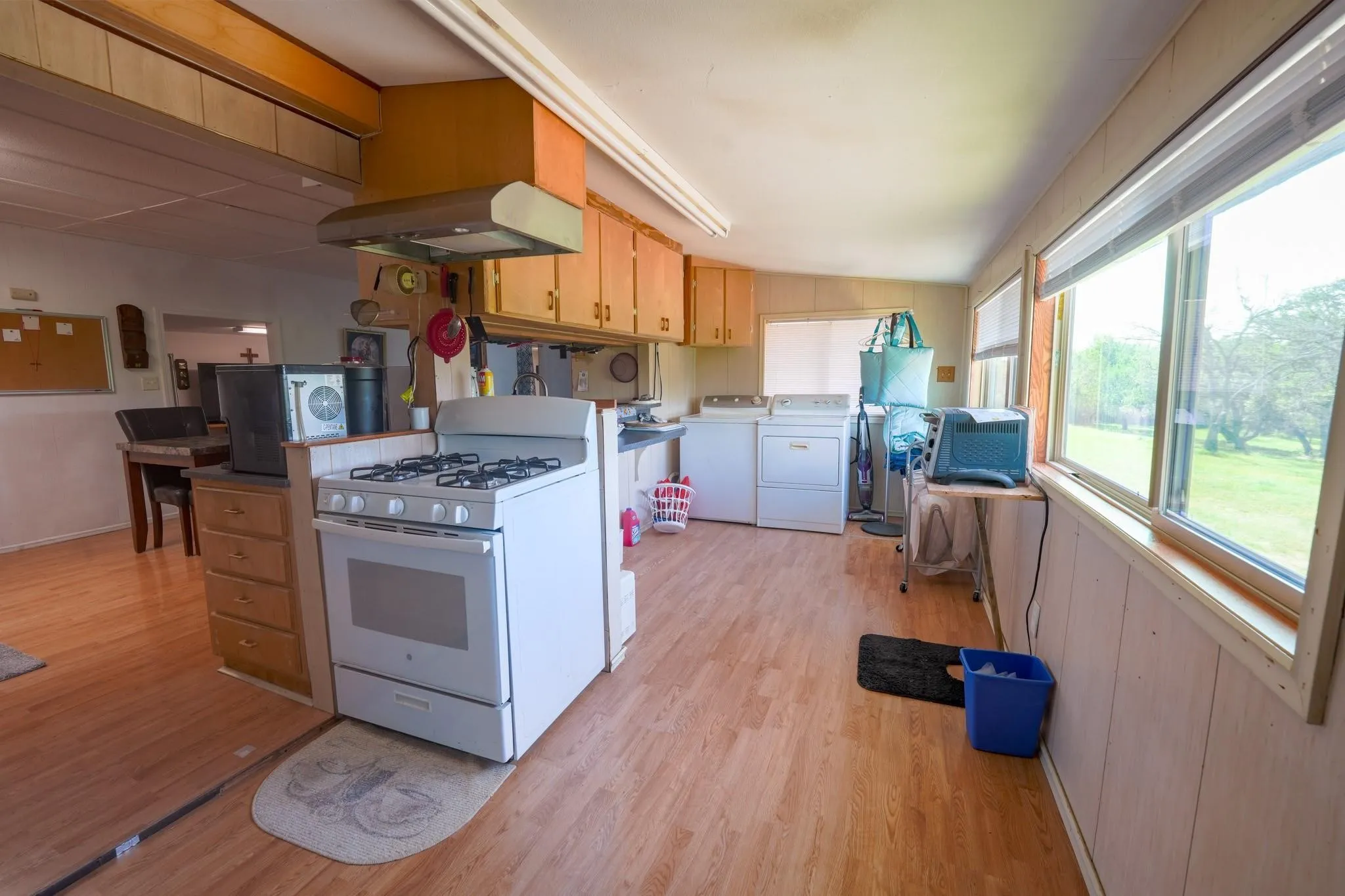 Kitchen featuring wood-finish flooring, light wood cabinetry, a white gas range, and large windows