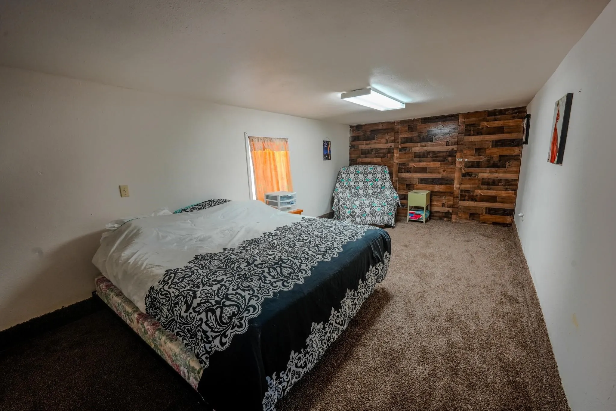 Spacious room featuring a prominent wood-panel accent wall, neutral carpet flooring, and white painted walls