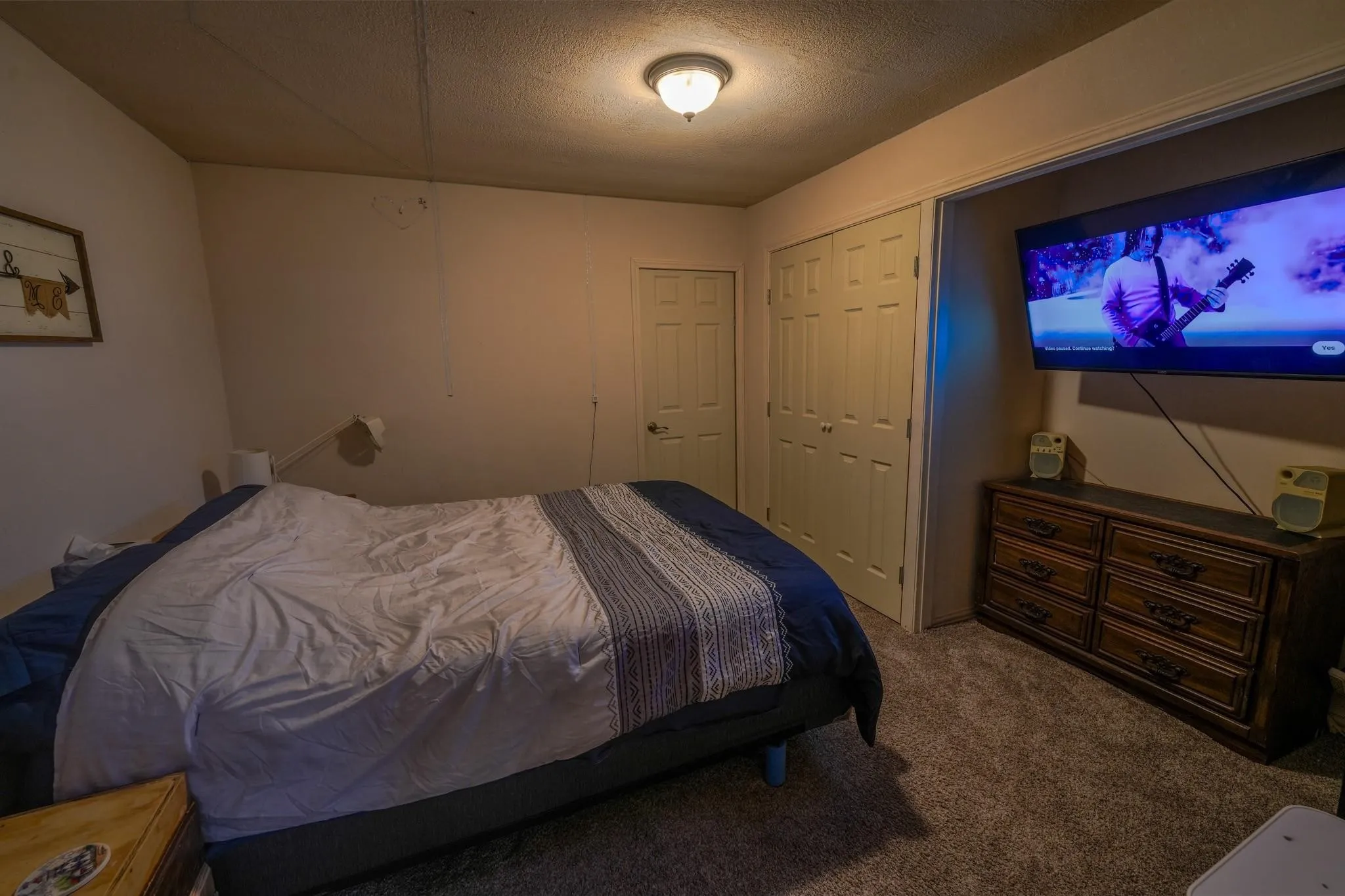 Carpeted room with a ceiling-mounted light fixture, featuring a door with a white finish, and a closet with bi-fold doors