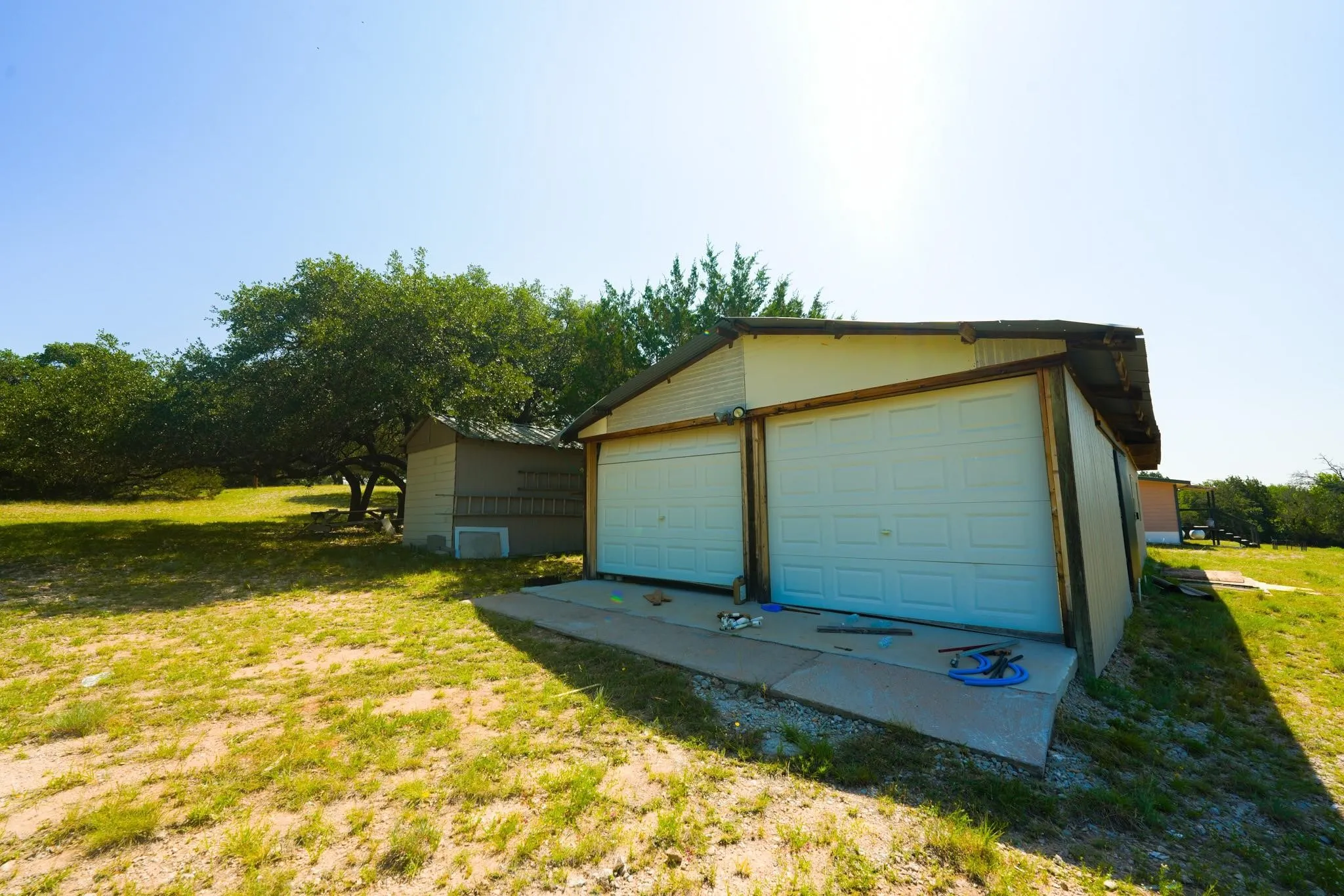 Detached two-car garage with white paneled doors and an adjacent utility shed, set on a grassy lot