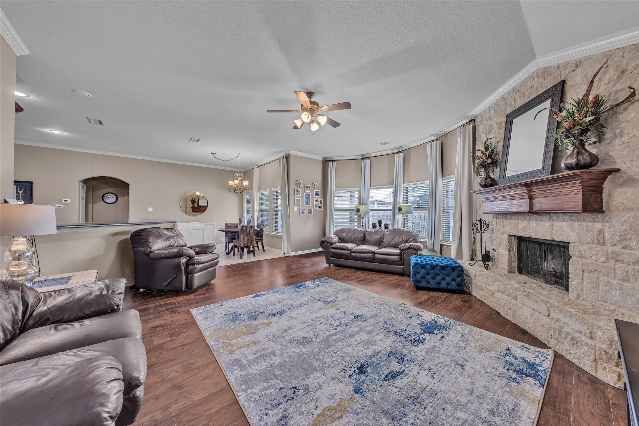Living area featuring a stone-clad fireplace with a wood mantel, wood-finish flooring, and a ceiling fan with integrated lighting