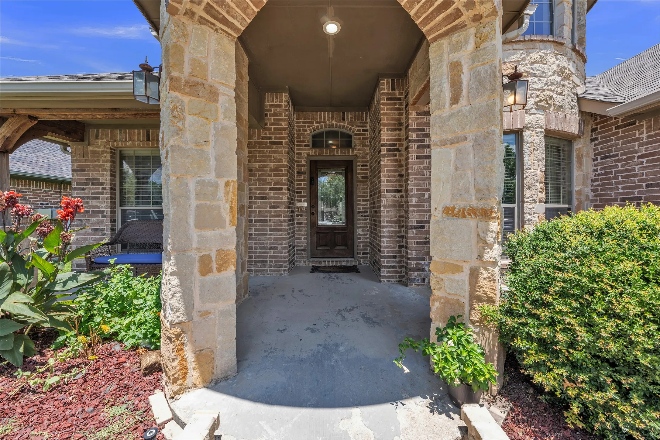 Covered entry featuring a dark wood door with decorative glass, flanked by stone columns and brick facade