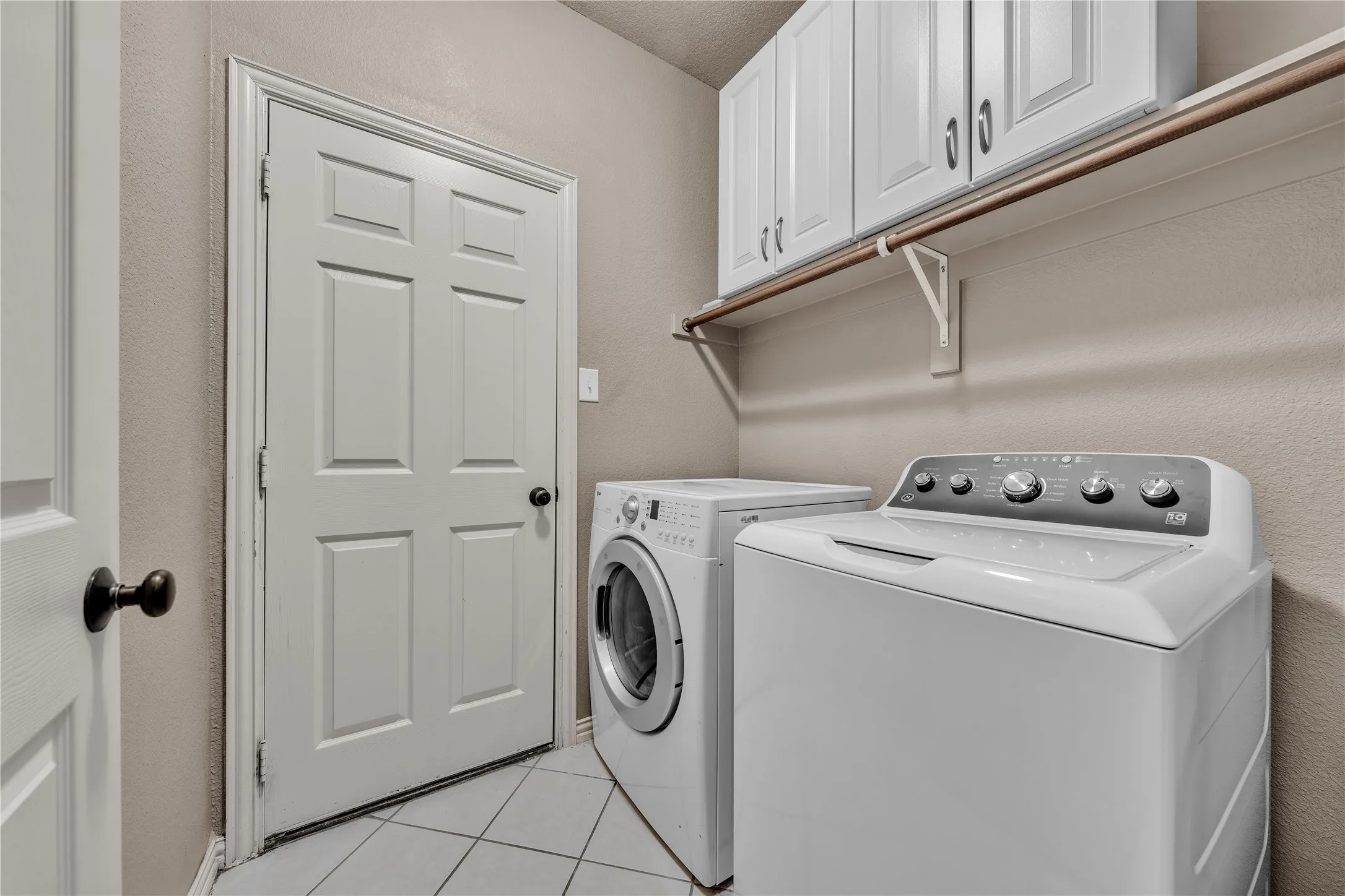 Dedicated utility area featuring white paneled doors, white upper cabinetry with brushed nickel hardware, and a durable tile floor